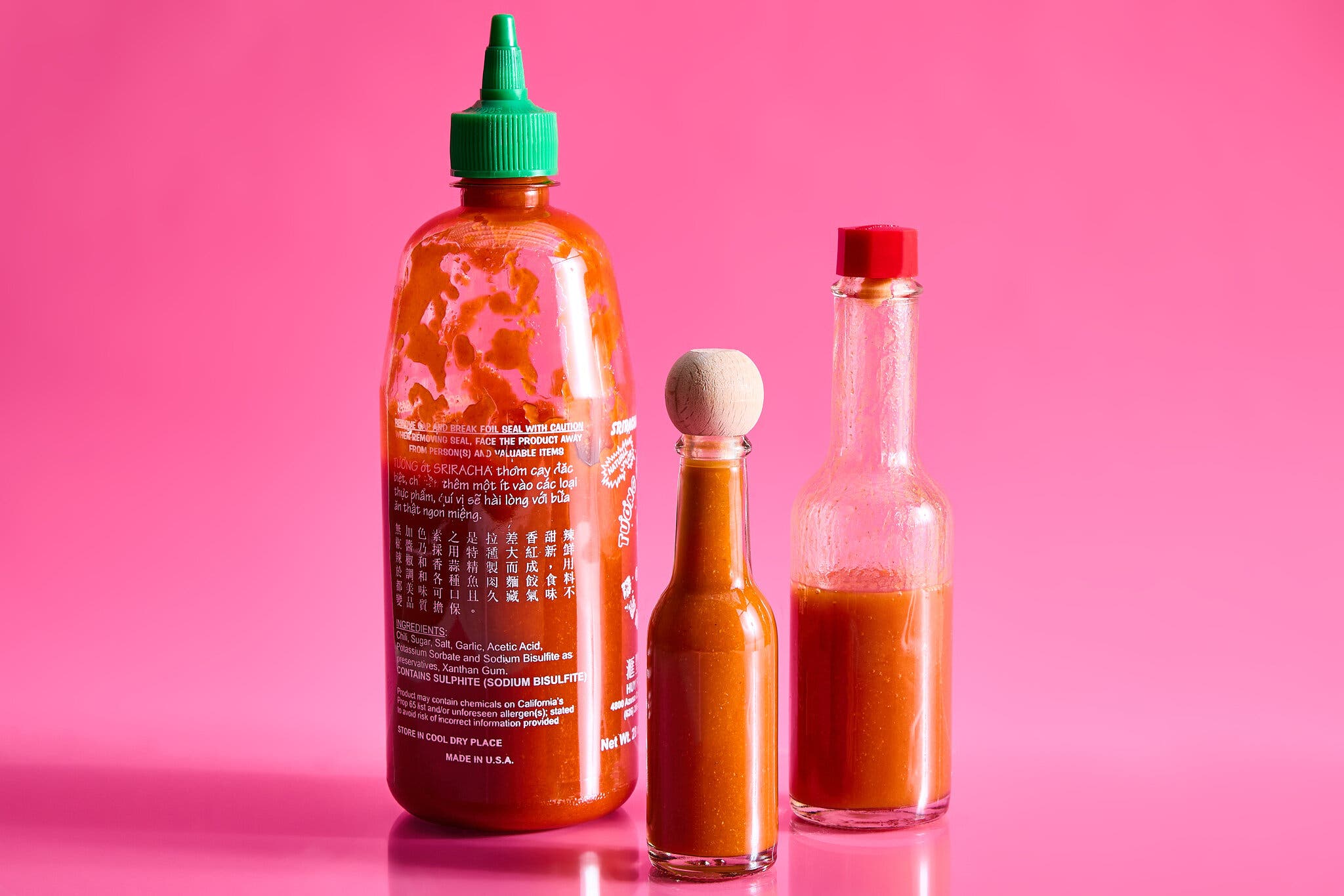 Three bottles of hot sauce against a hot pink background.