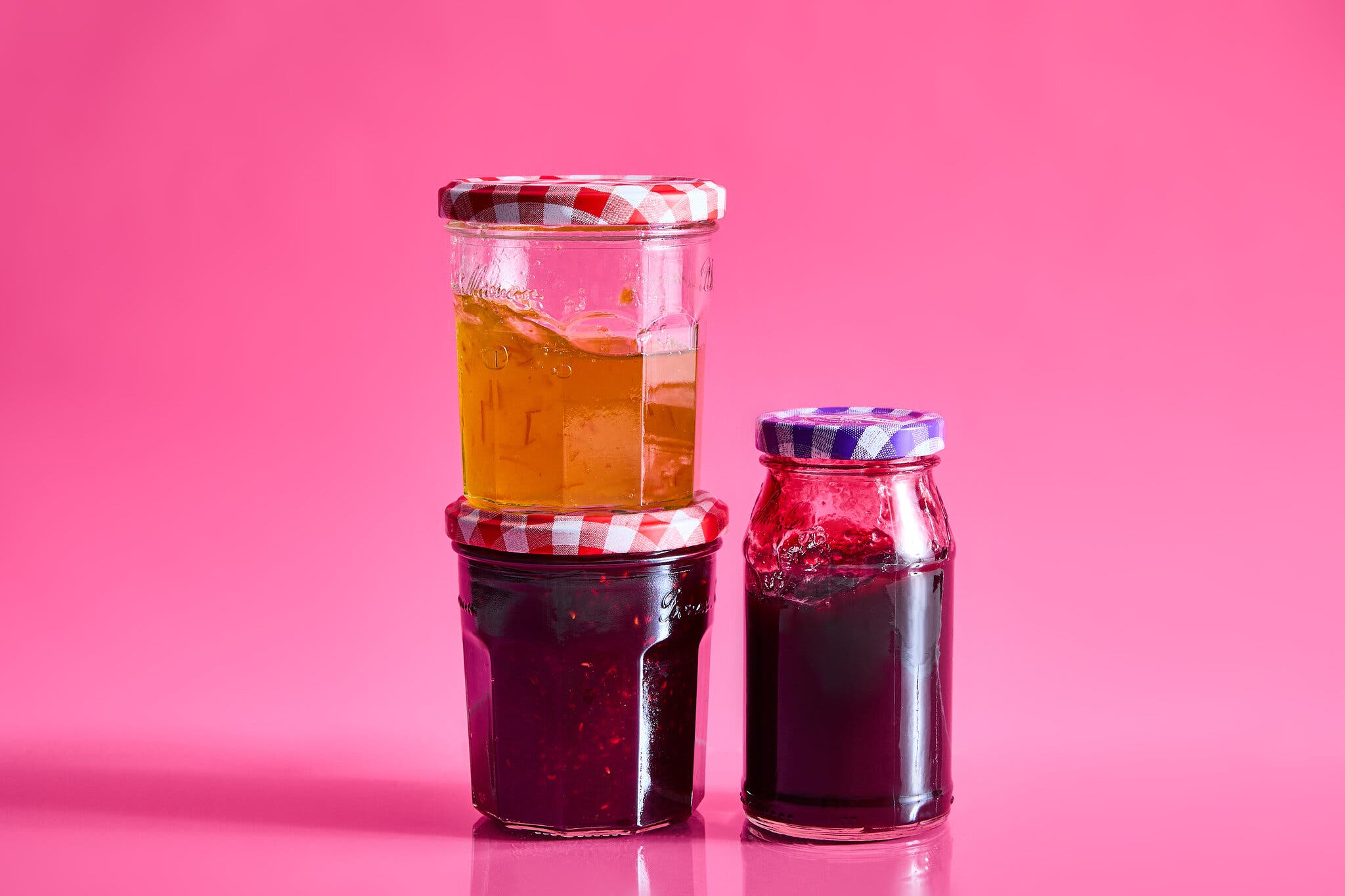 Three jars of jelly against a hot pink background.