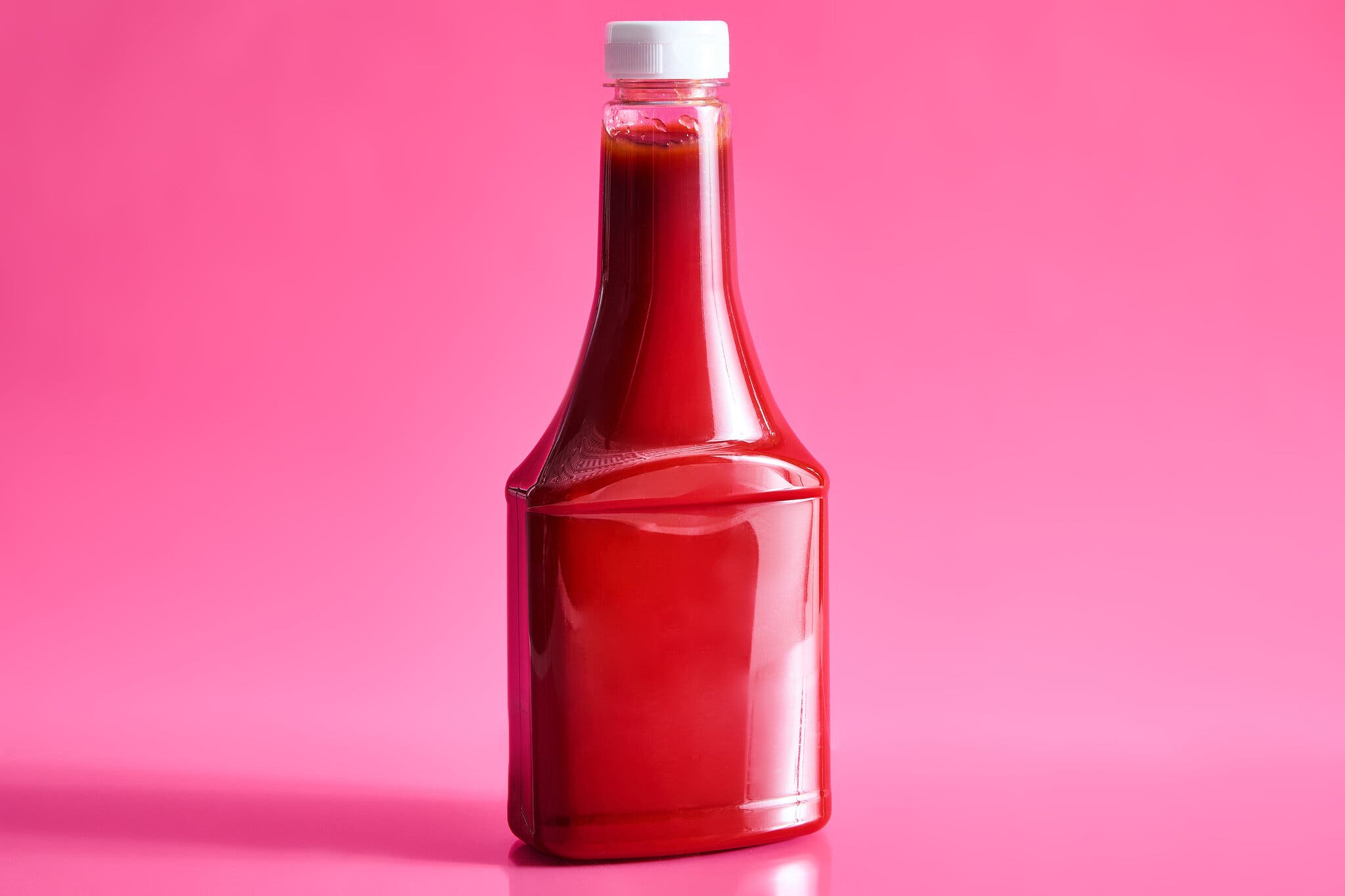 An unlabeled bottle of ketchup against a hot pink background.