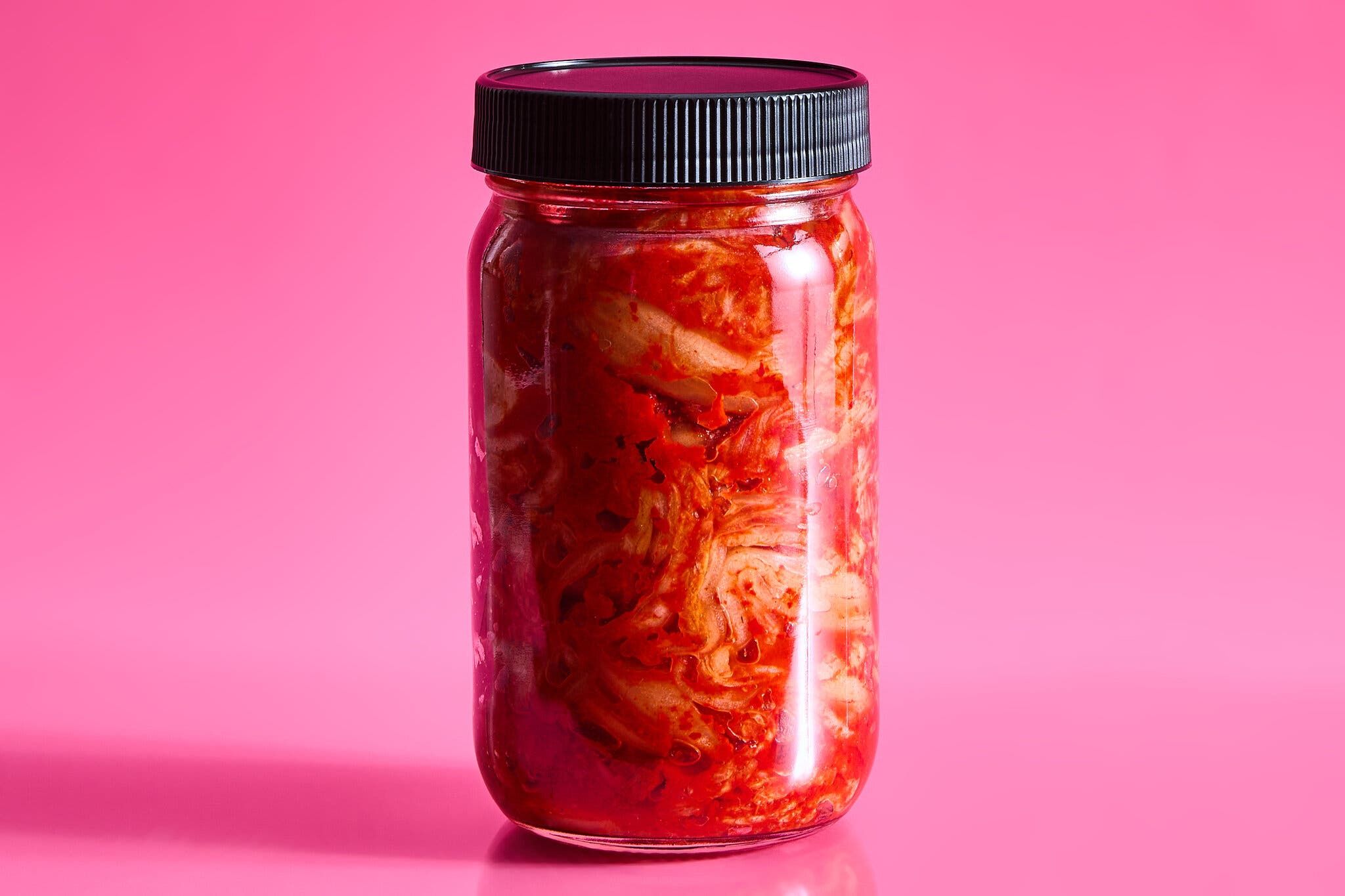 An unlabeled jar of kimchi against a hot pink background.