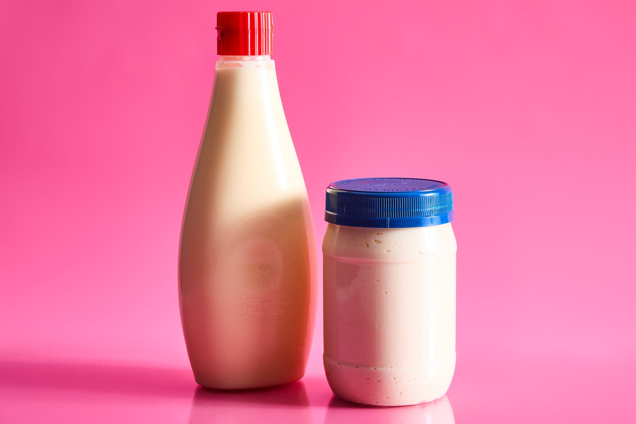 A bottle and a jar of mayonnaise against a hot pink background.
