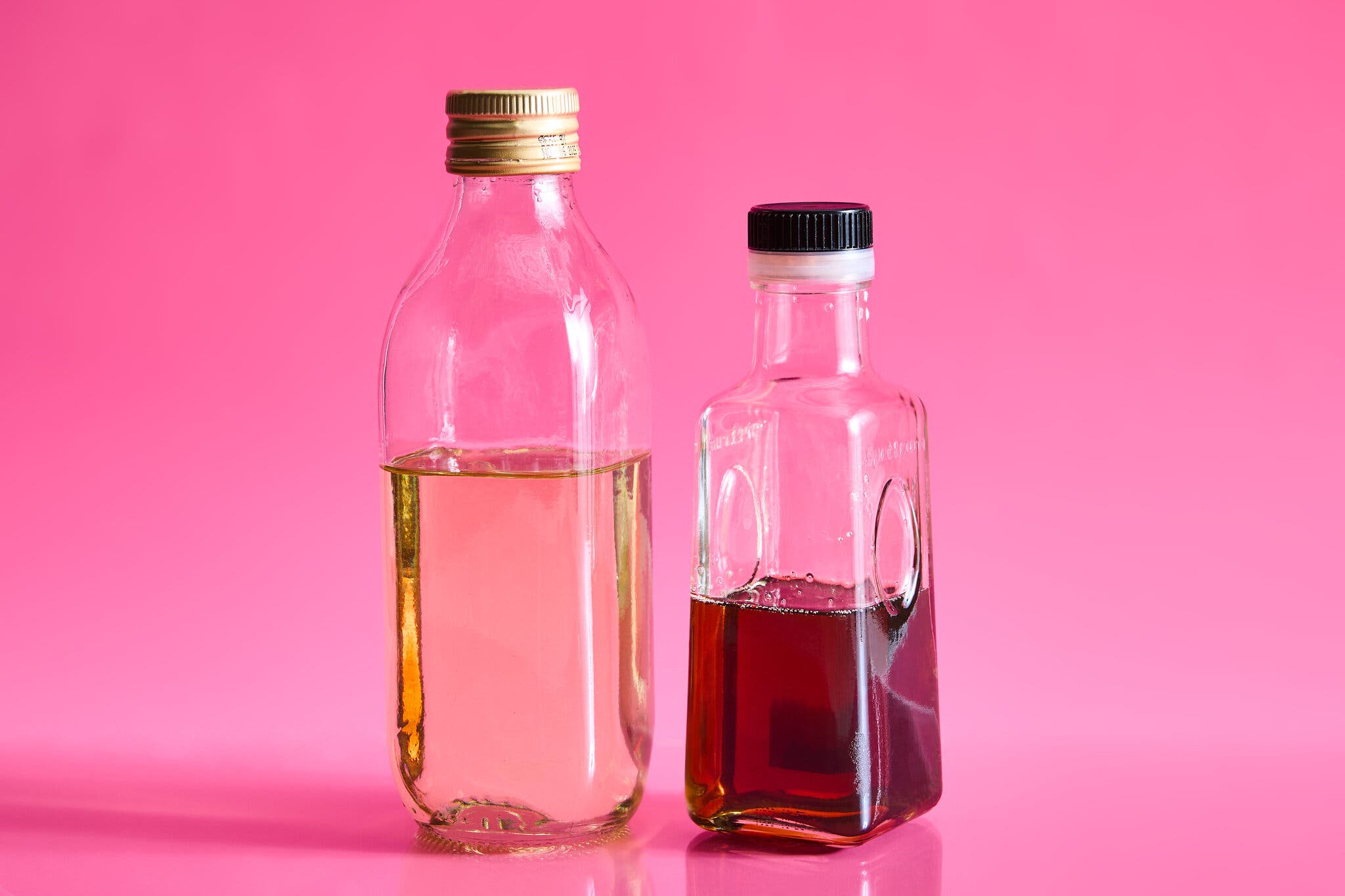 Two bottles of oil — one lighter and one darker in color — against a hot pink background.