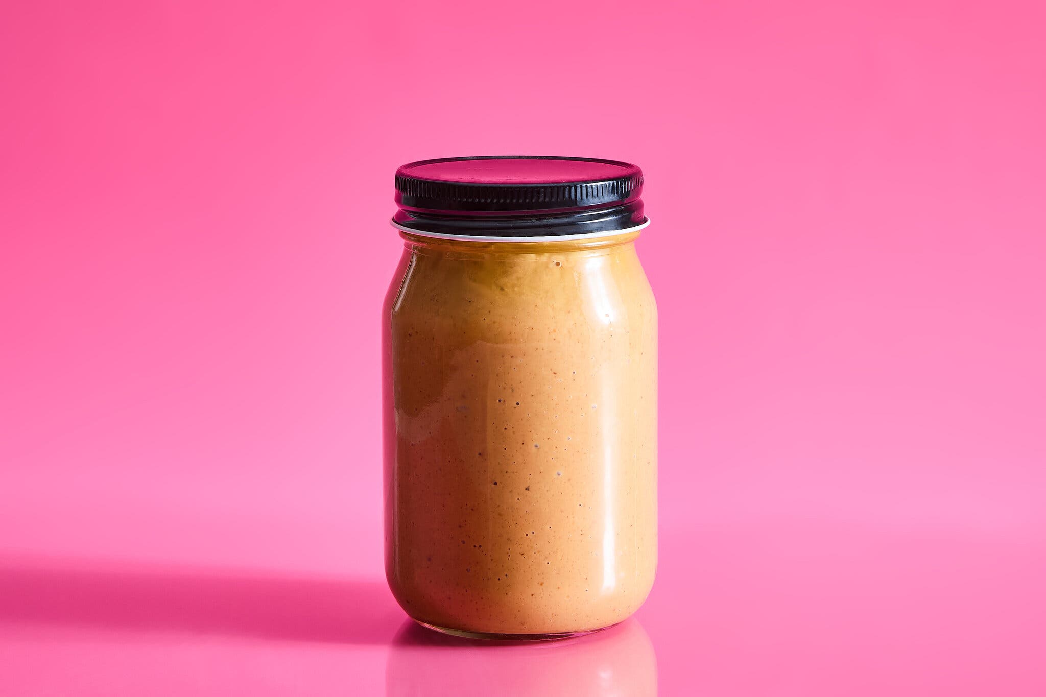 A jar of peanut butter against a hot pink background.