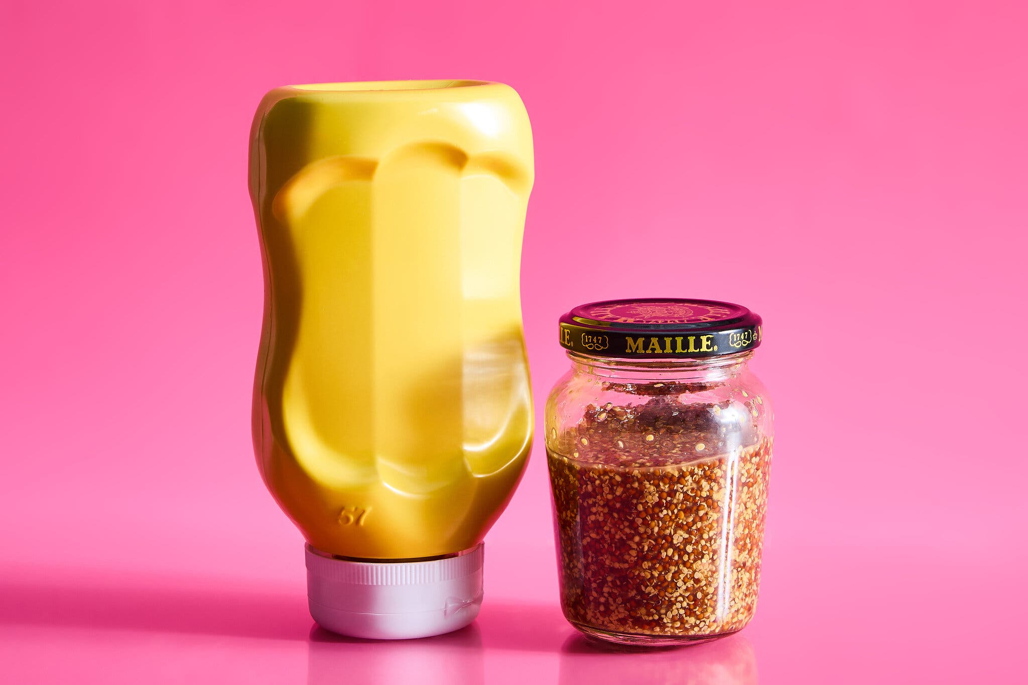 A bottle of yellow mustard and a jar of stone-ground mustard against a hot pink background.