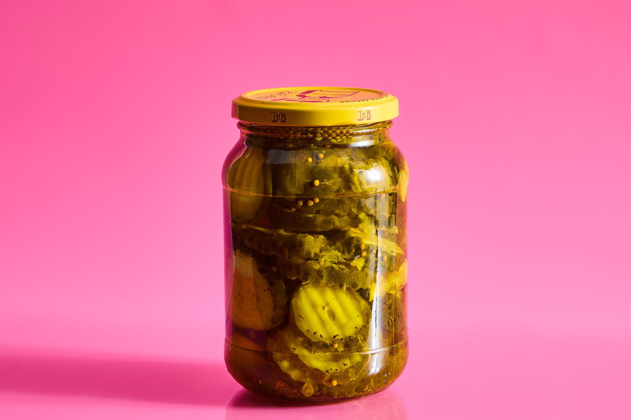 A jar of sliced pickles against a hot pink background.