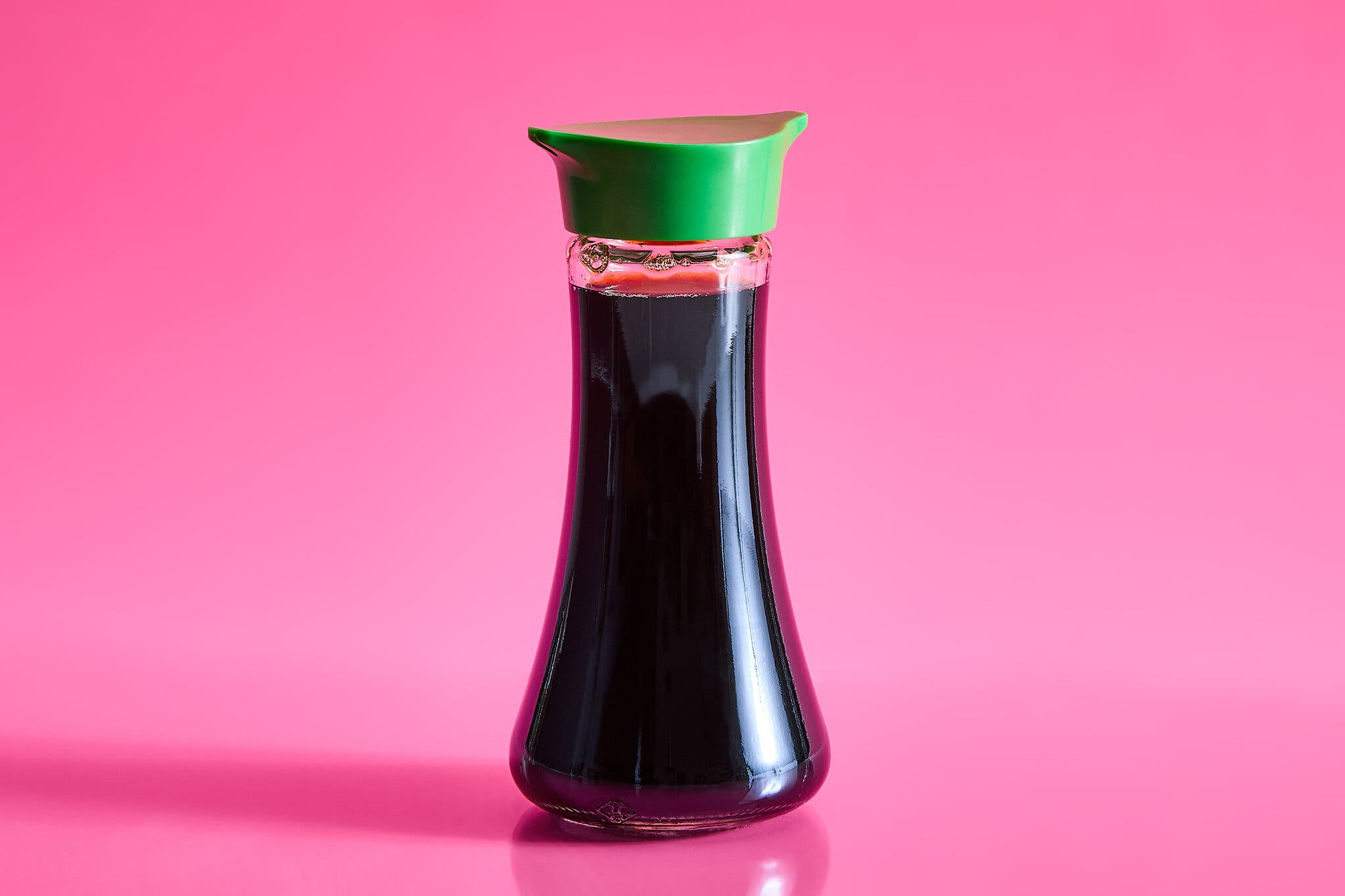 A bottle of soy sauce against a hot pink background.