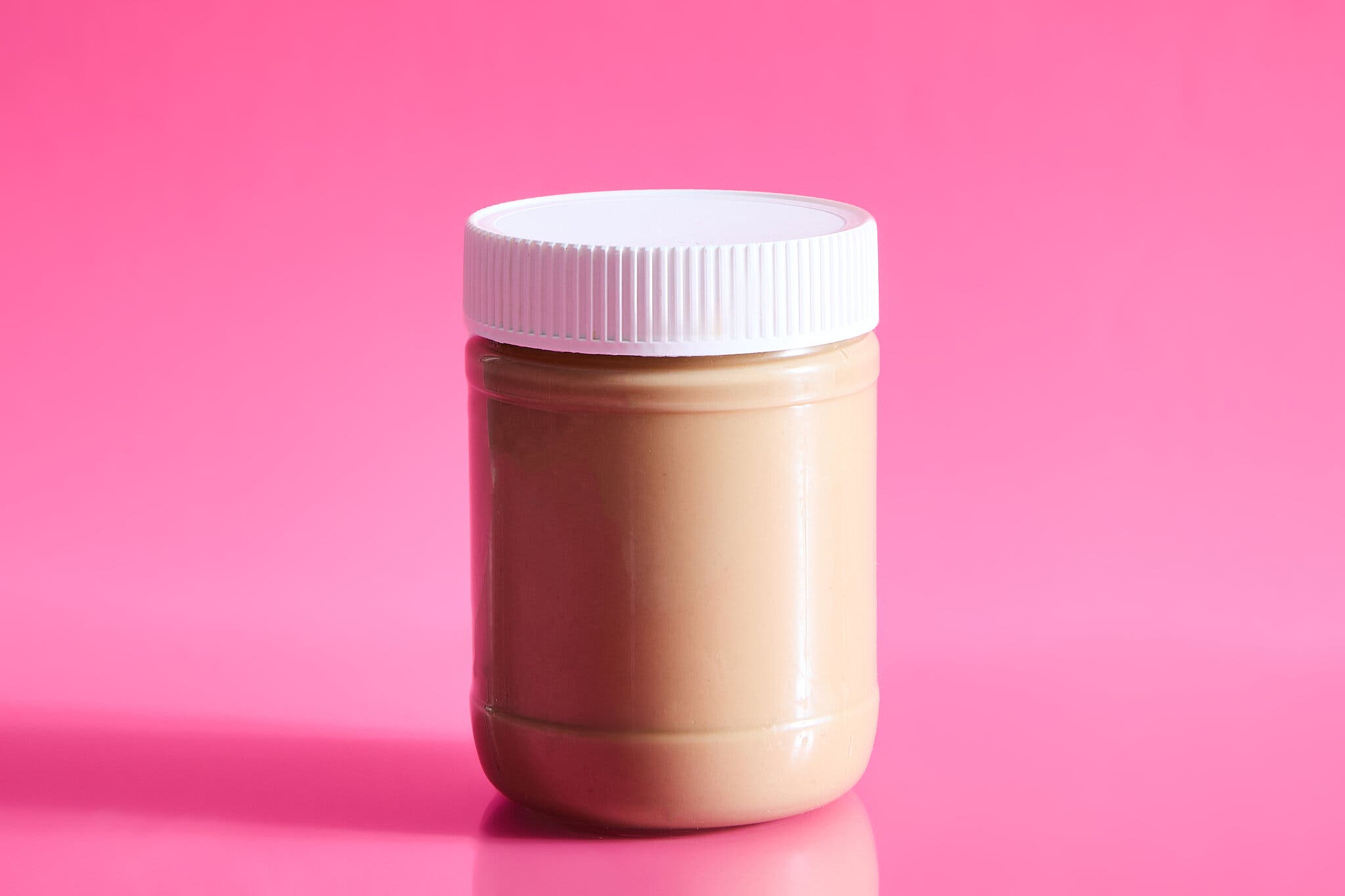 An unlabeled jar of tahini against a hot pink background.