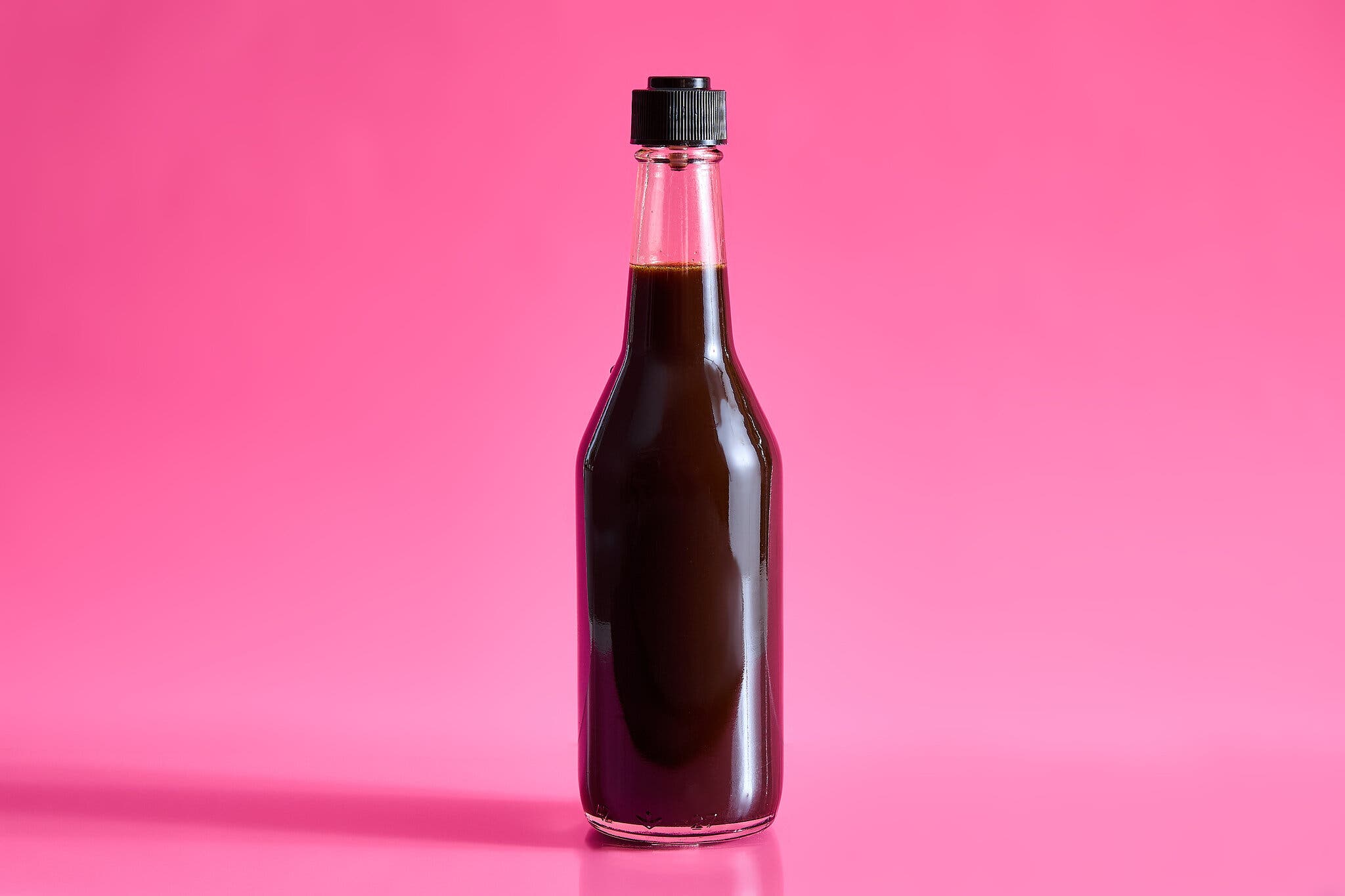 A bottle of Worcestershire sauce against a hot pink background.