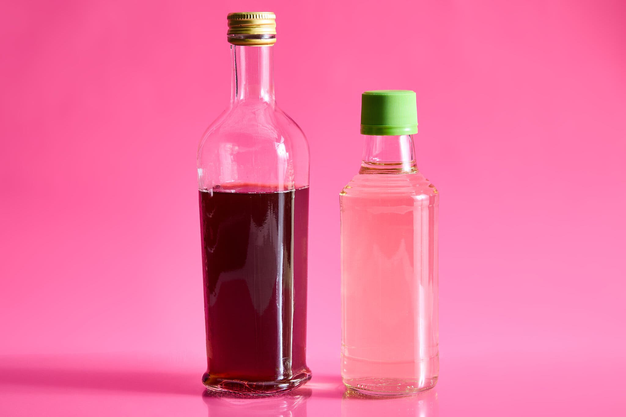 Two bottles, one of dark vinegar and another of light, against a hot pink background.