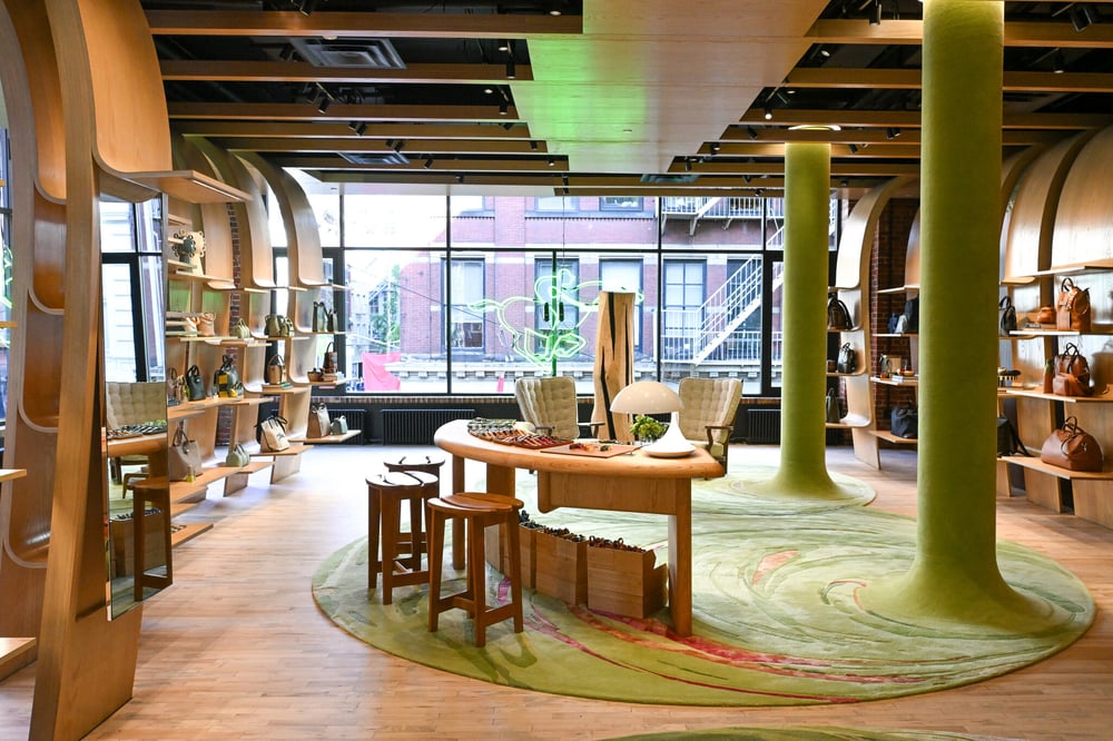 Inside Longchamp's La Maison Unique: fluid architecture, curved display shelving and green-patterned rugs create a serene, mid-century inspired retail space.