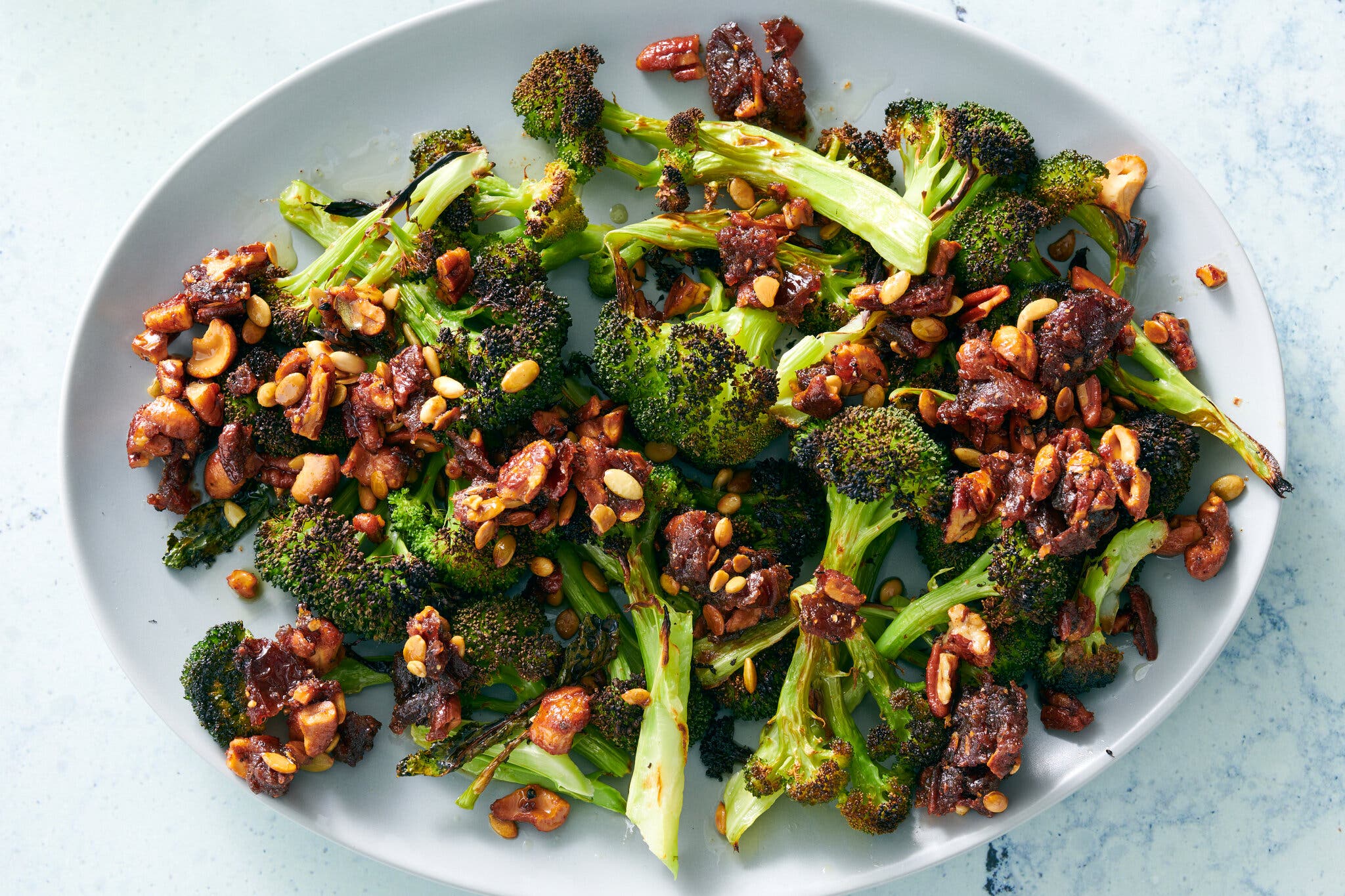 An oval white platter holds broccoli with sizzled nuts and dates.