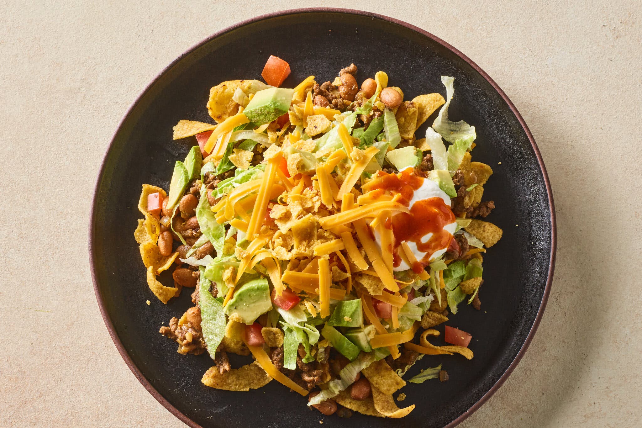 An overhead image of a bowl topped with lettuce, cheese, tortilla chips and beans.