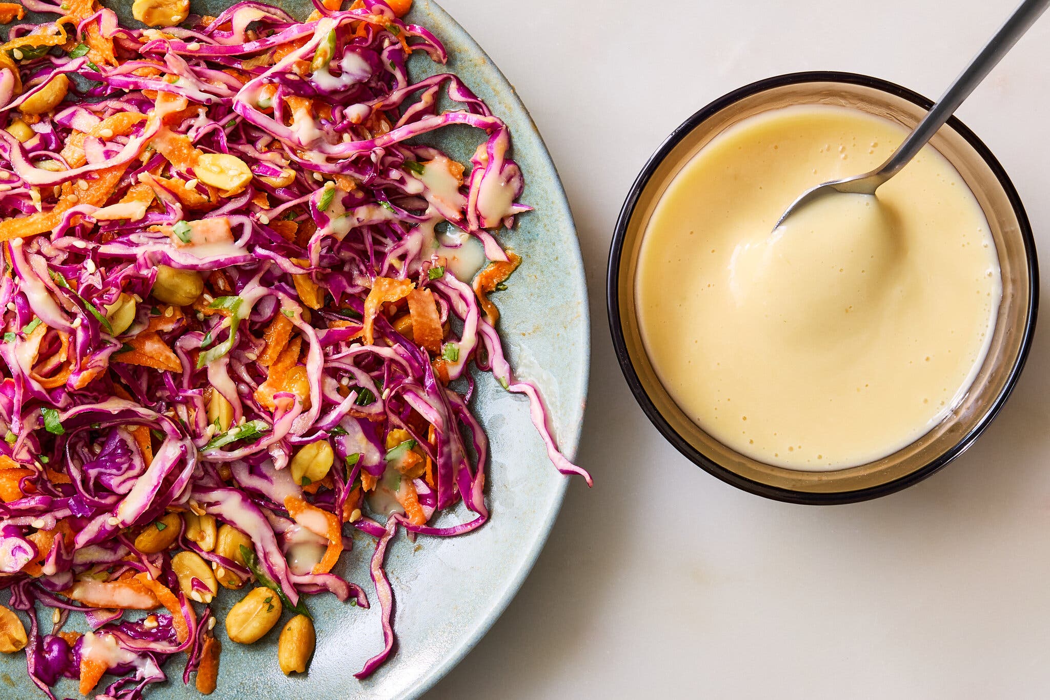 An overhead image of a bowl of creamy ginger dressing next to a plate of shredded cabbage.