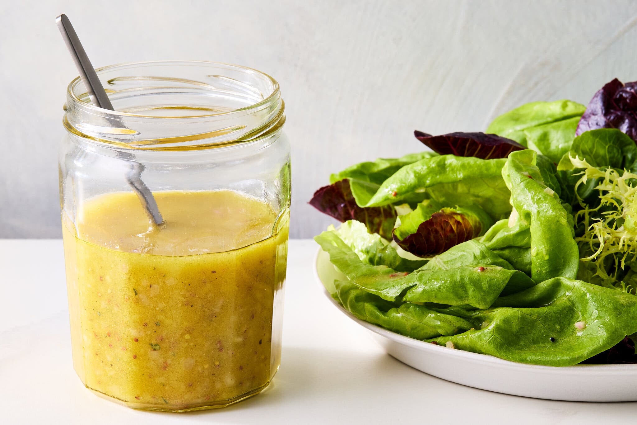 A side image of a jar filled with a golden dressing next to a green salad.