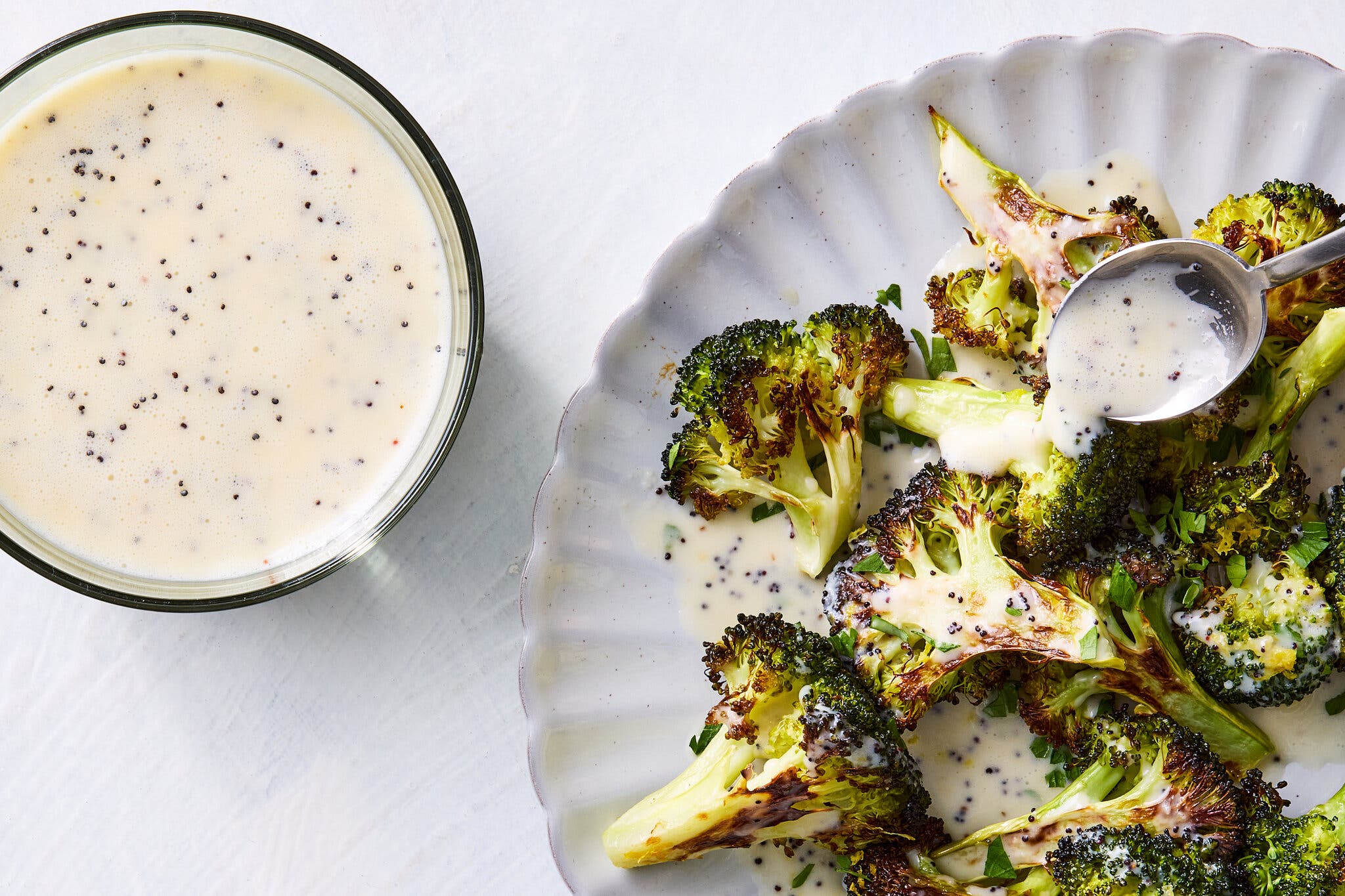 An overhead image of a creamy dressing in a bowl next to a plate topped with broccoli.