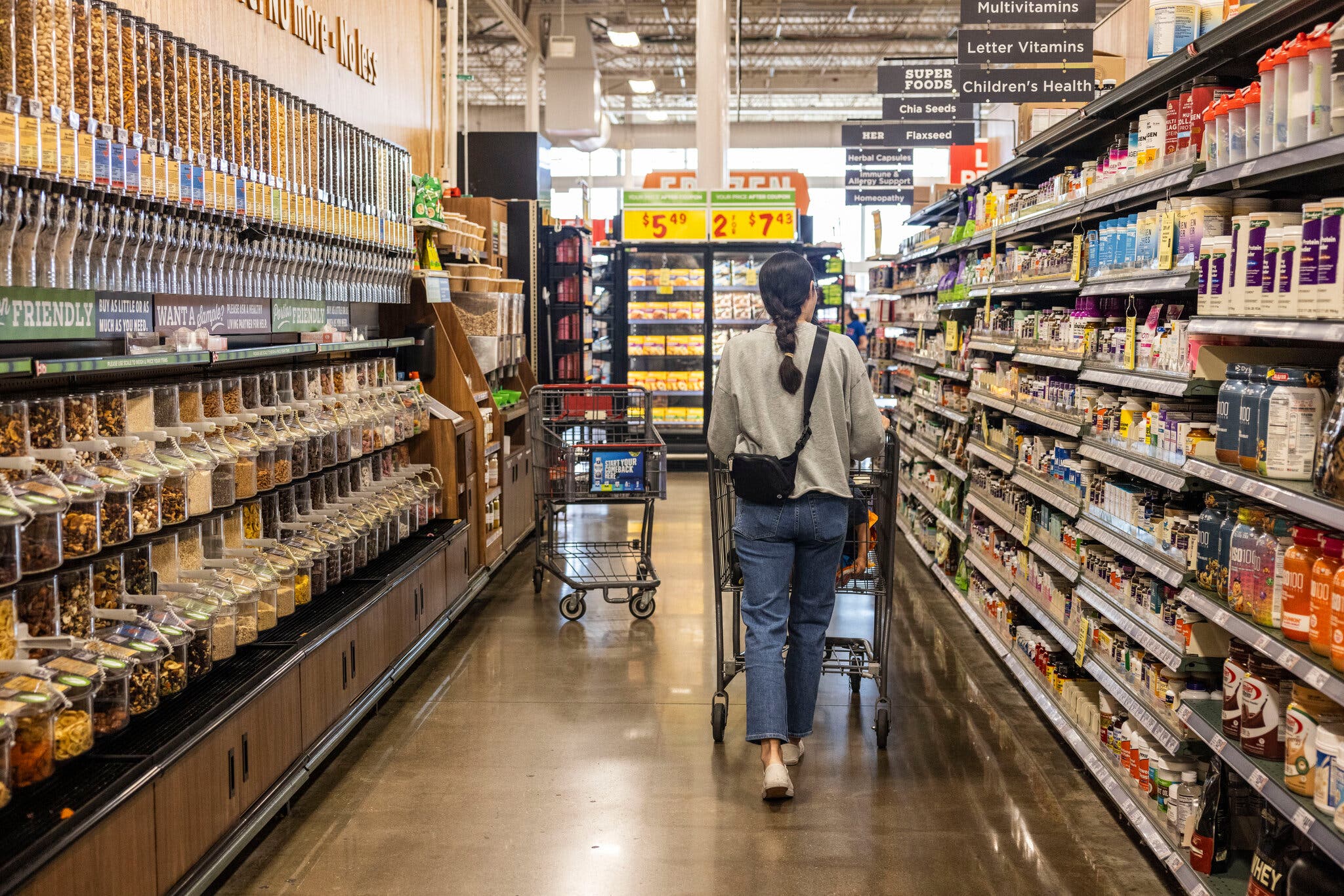 A woman pushes a shopping cart, browsing the aisles of a grocery store.