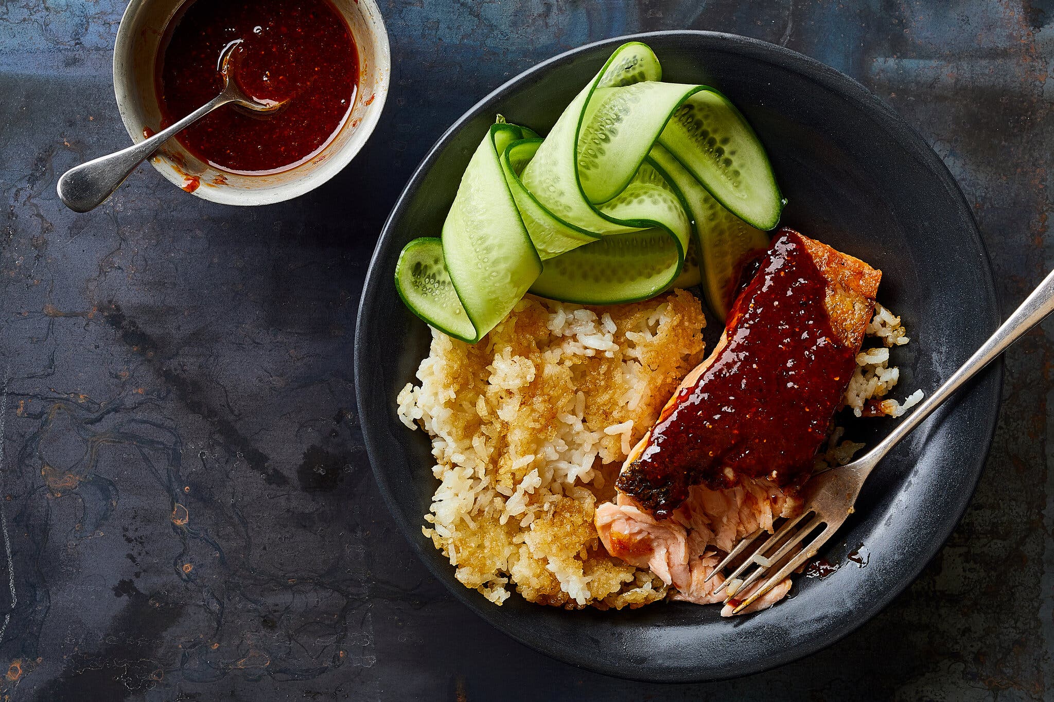 A black bowl is filled with rice, salmon and curled slices of cucumber.