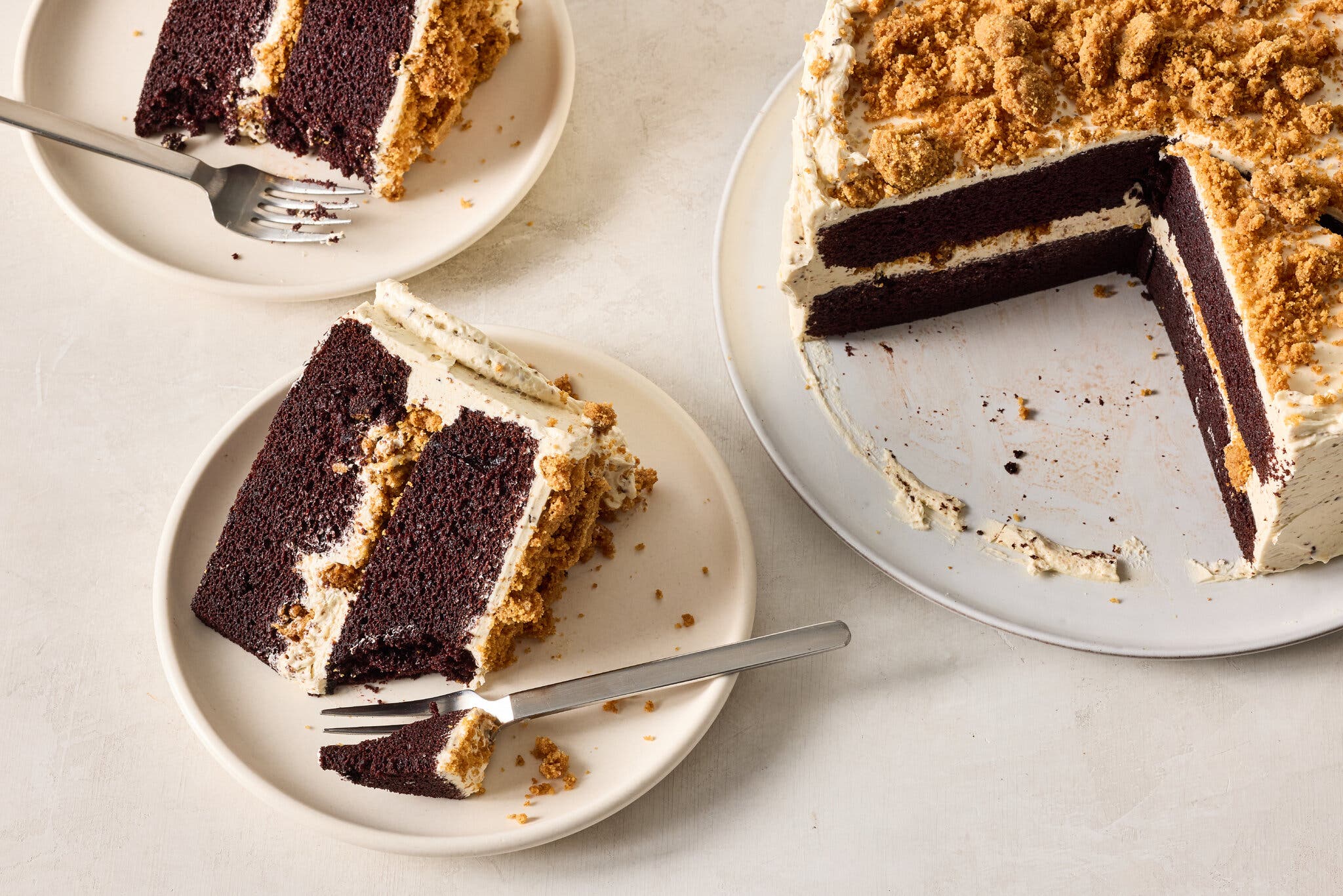 A two-layer chocolate cake with toasted marshmallow buttercream and graham cracker crumbles on top. To the left of the frame, two slices of cake on small white plates with forks.