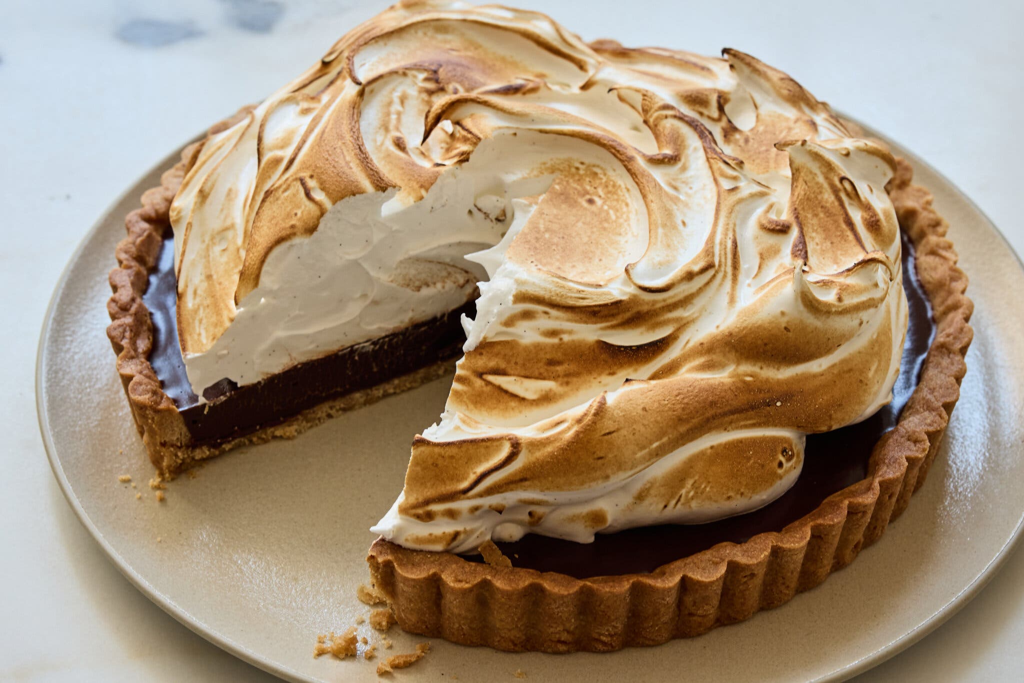 A stunning chocolate tart topped with a torched meringue with a slice missing.