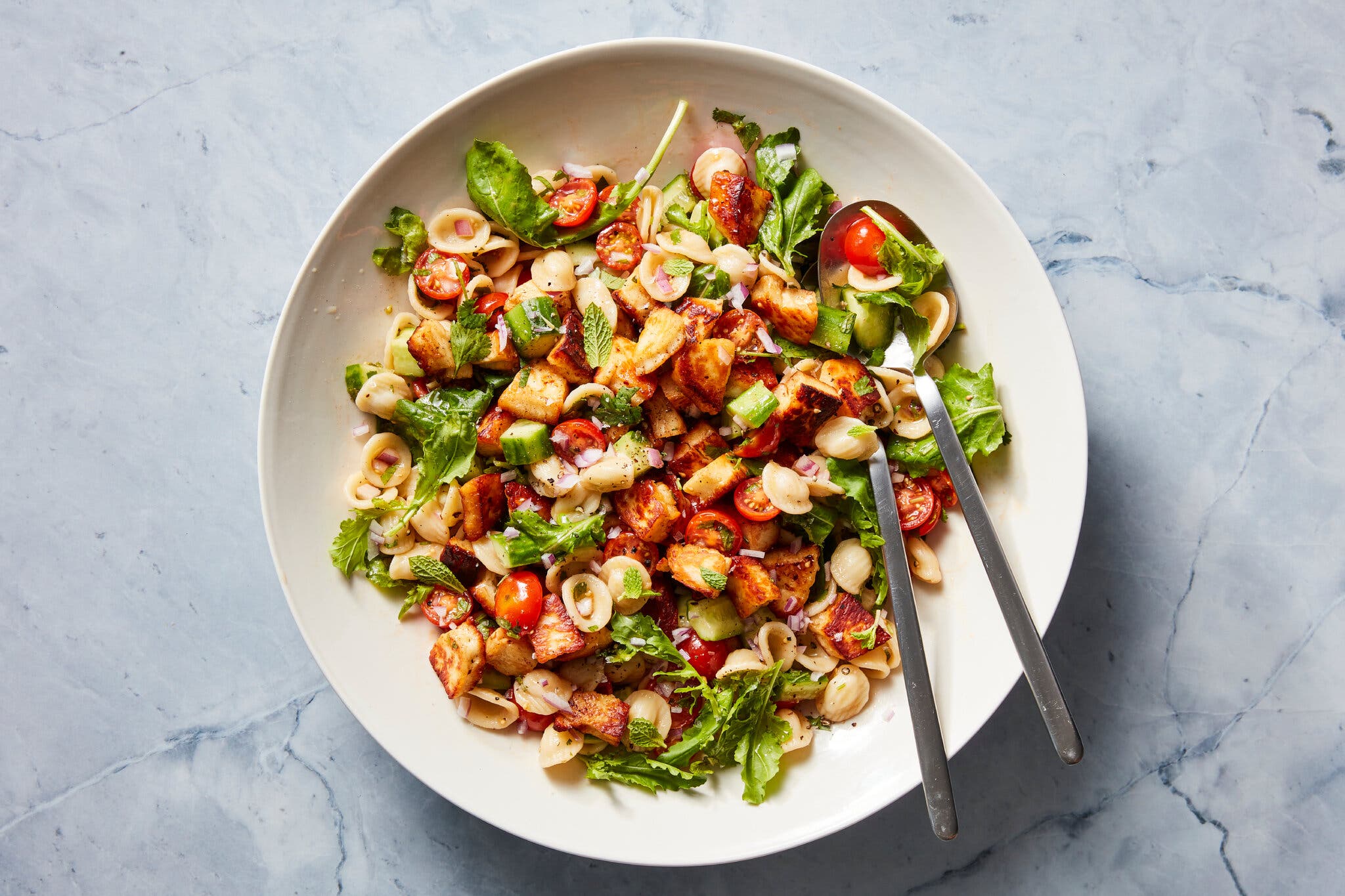 An overhead image of pasta paired with fried halloumi cubes, tomatoes and cucumbers.