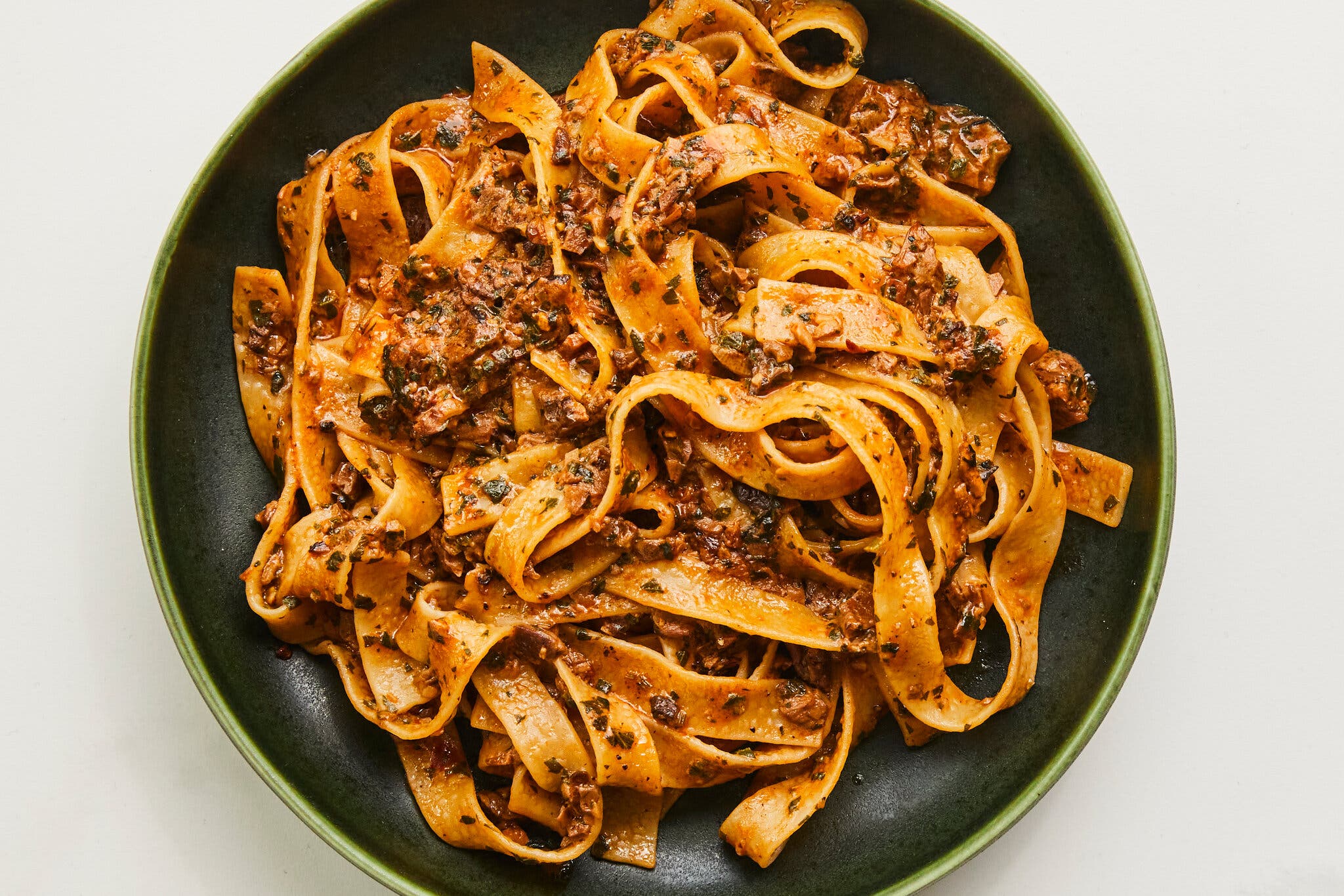An overhead image of tagliatelle coated with a porcini ragu and in a black plate.