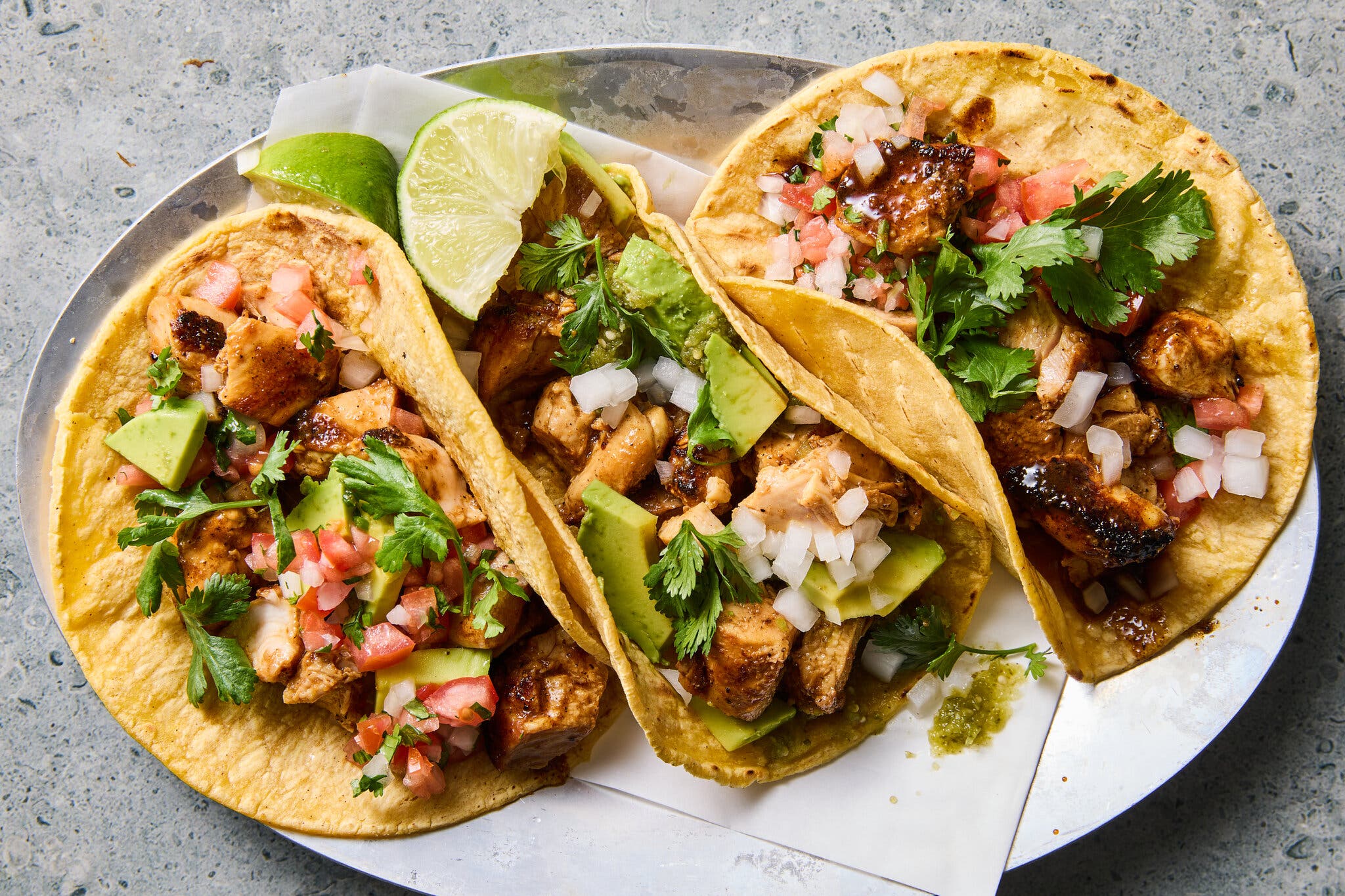 An overhead image of three tacos sitting open face and filled with chicken, avocado, herbs and onions.