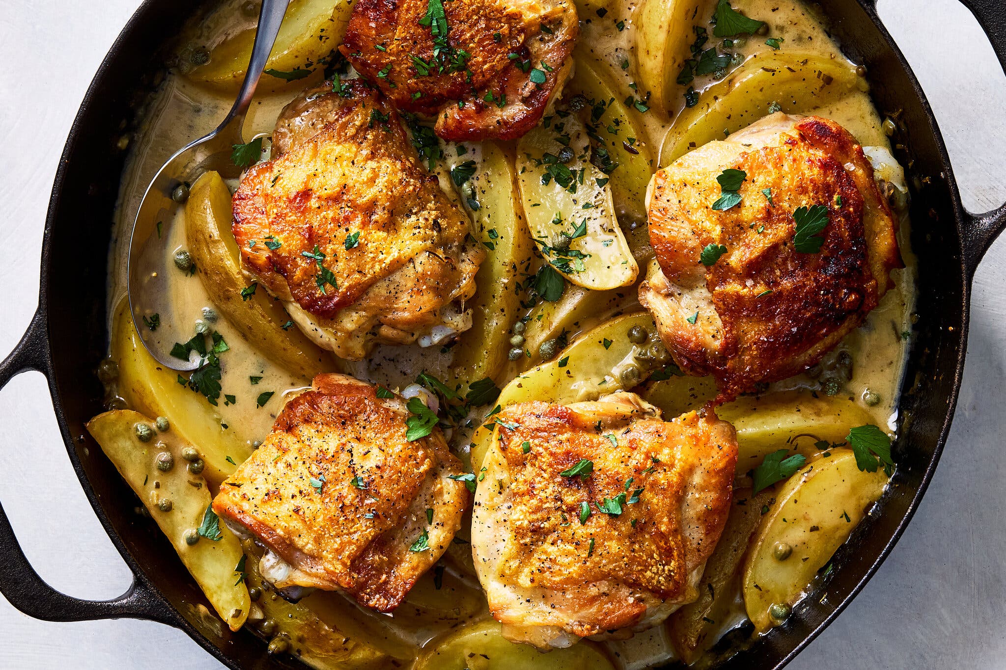 An overhead image of crisp chicken thighs on a bed of sauced potatoes.