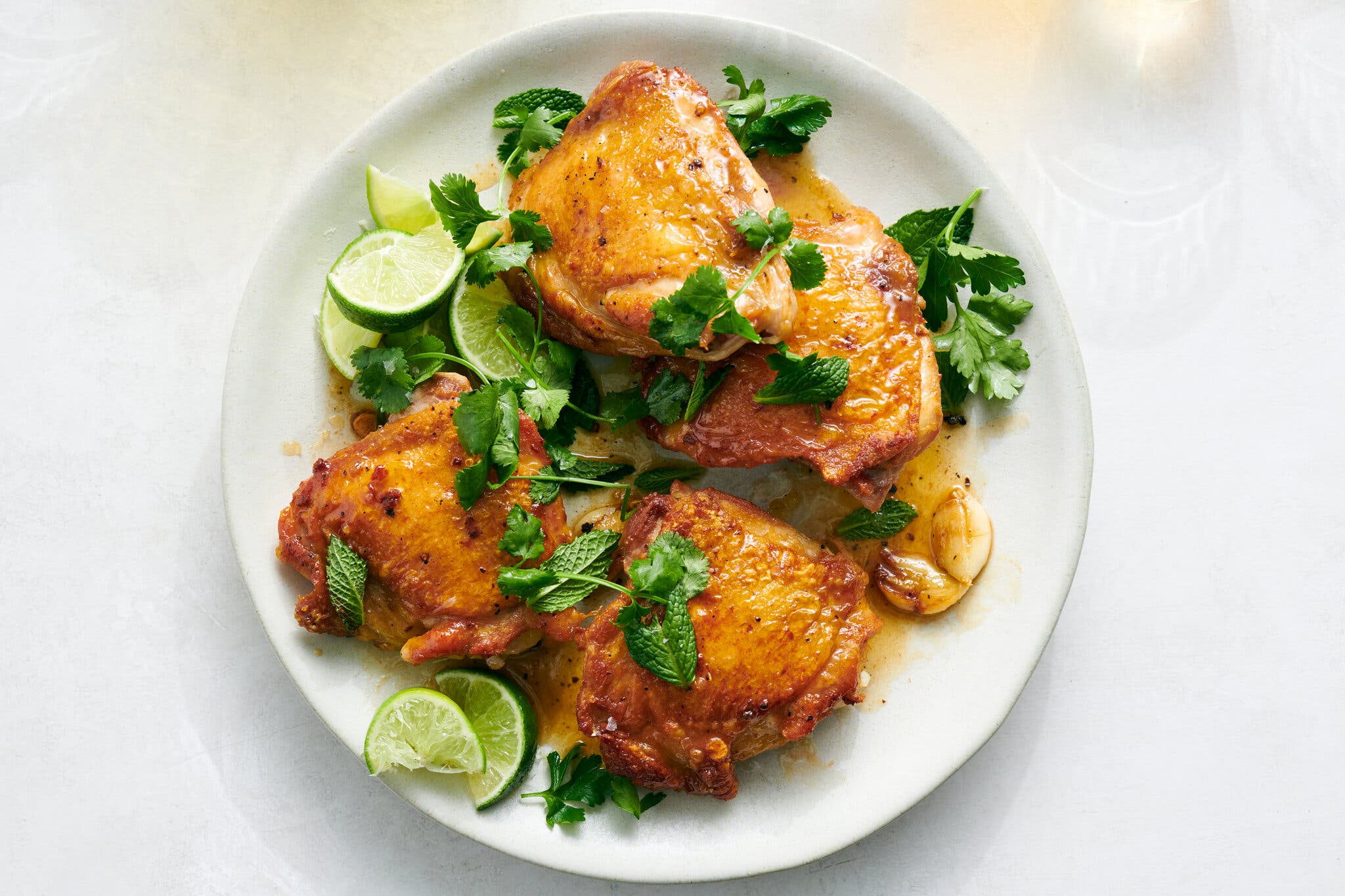 An overhead image of crispy chicken thighs next to spent lime wedges and topped with herbs.