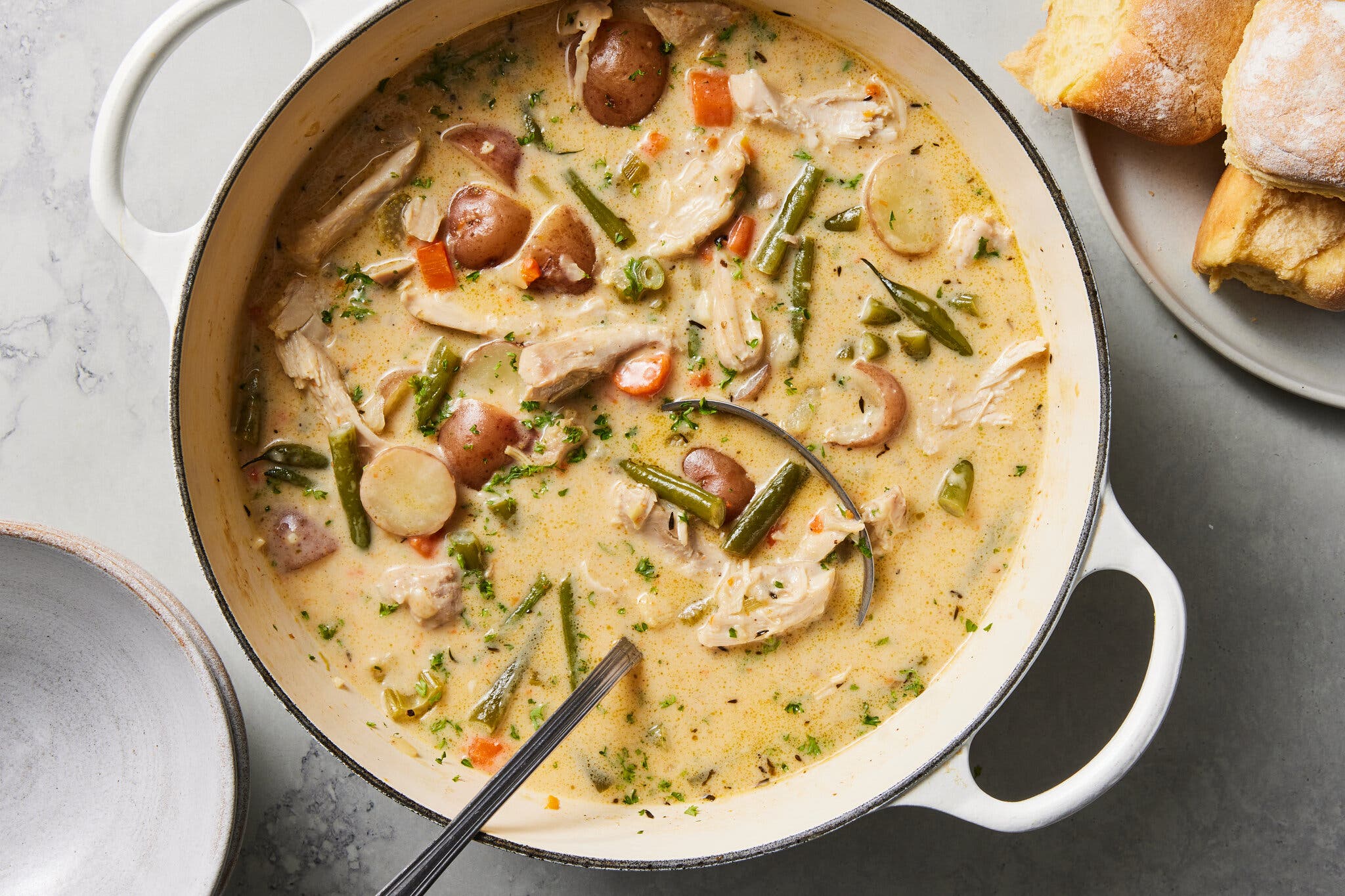 An overhead image of a Dutch oven filled with a chicken stew studded with potatoes and green beans.