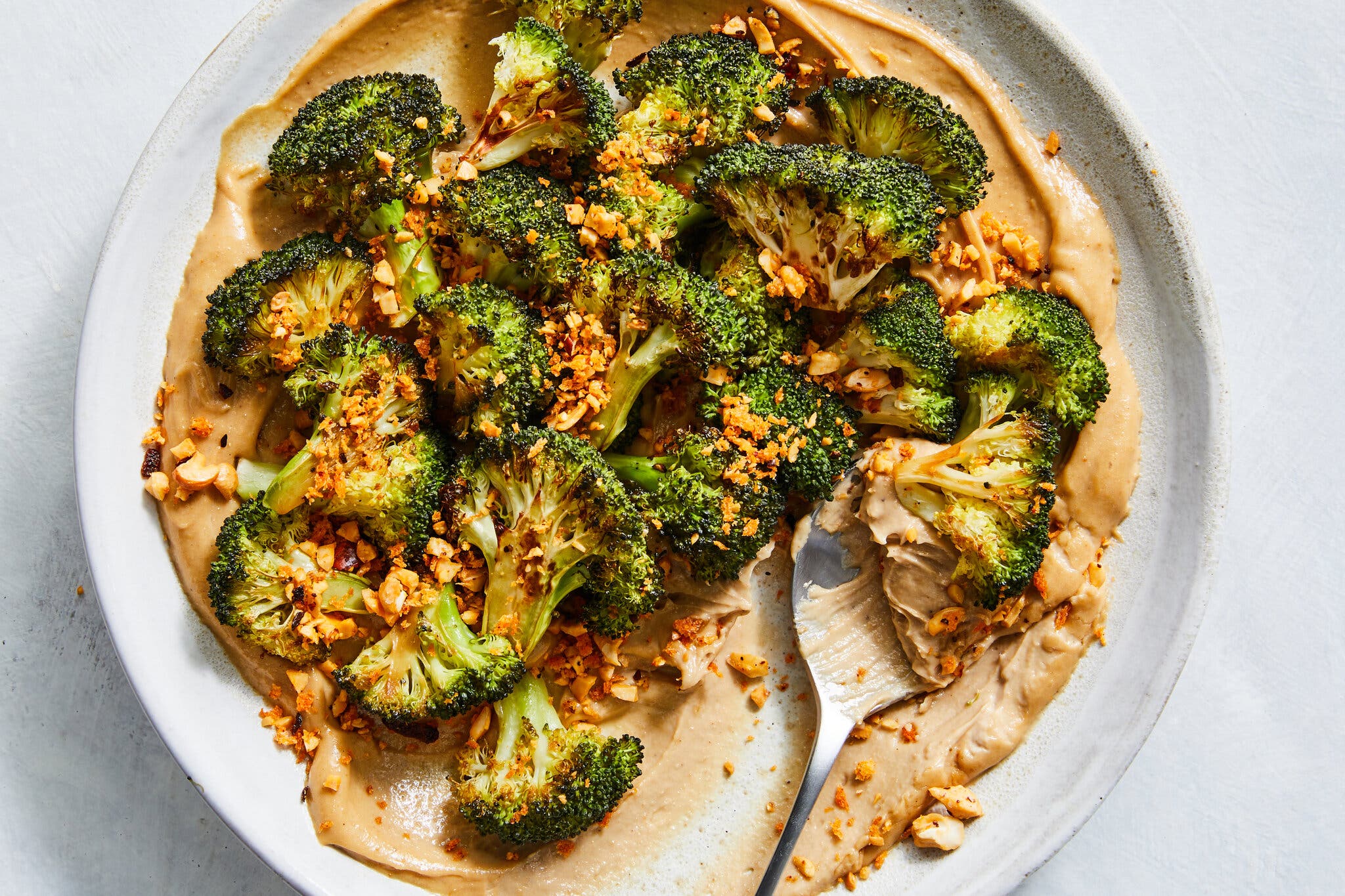 An overhead image of broccoli topped with nuts and chile crisp on a bed of creamy whipped tofu.