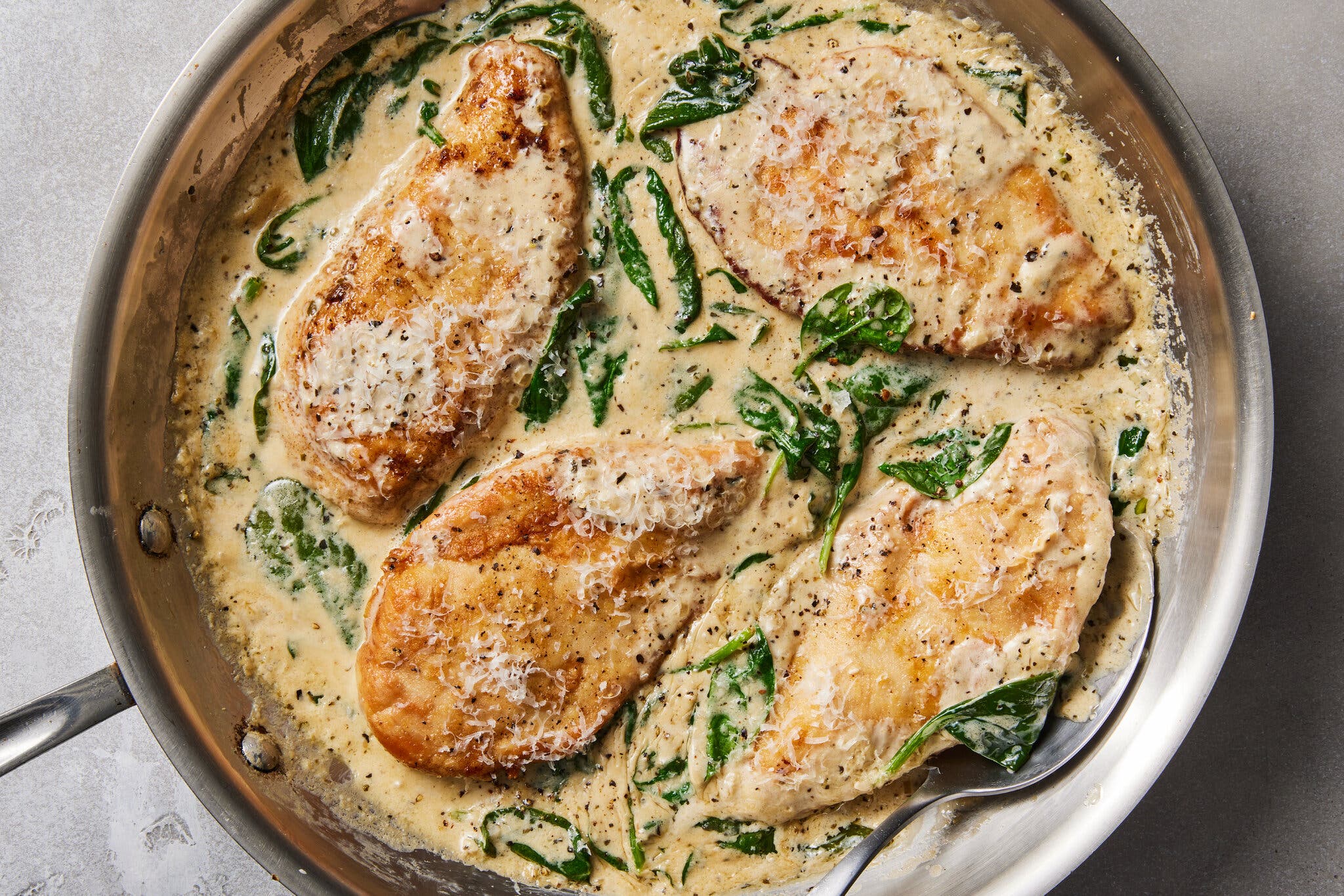 An overhead image of chicken breasts in a skillet filled with a creamy sauce and wilted spinach.