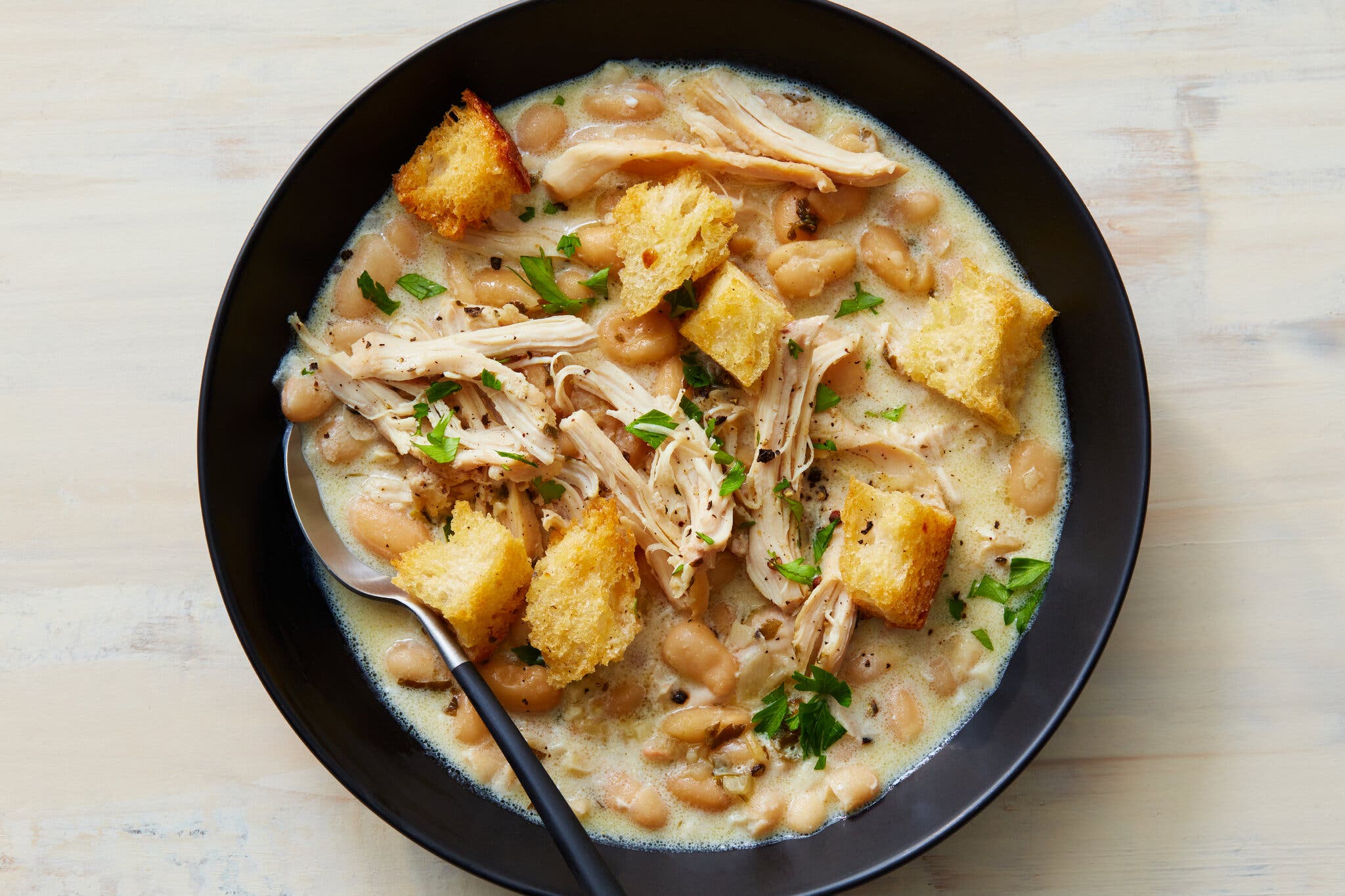 Croutons and shredded chicken top a bowl of a creamy bean soup.