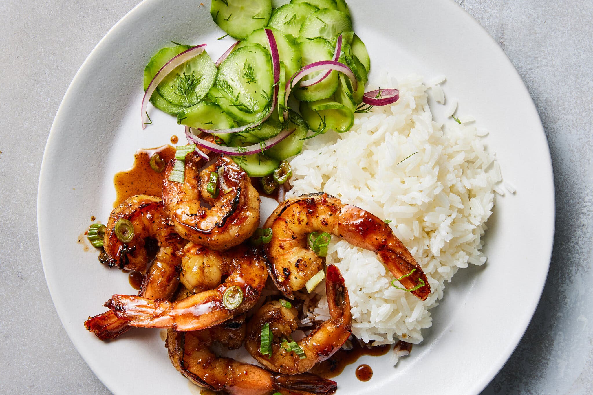 An overhead image of sauced shrimp next to rice and a cucumber salad.