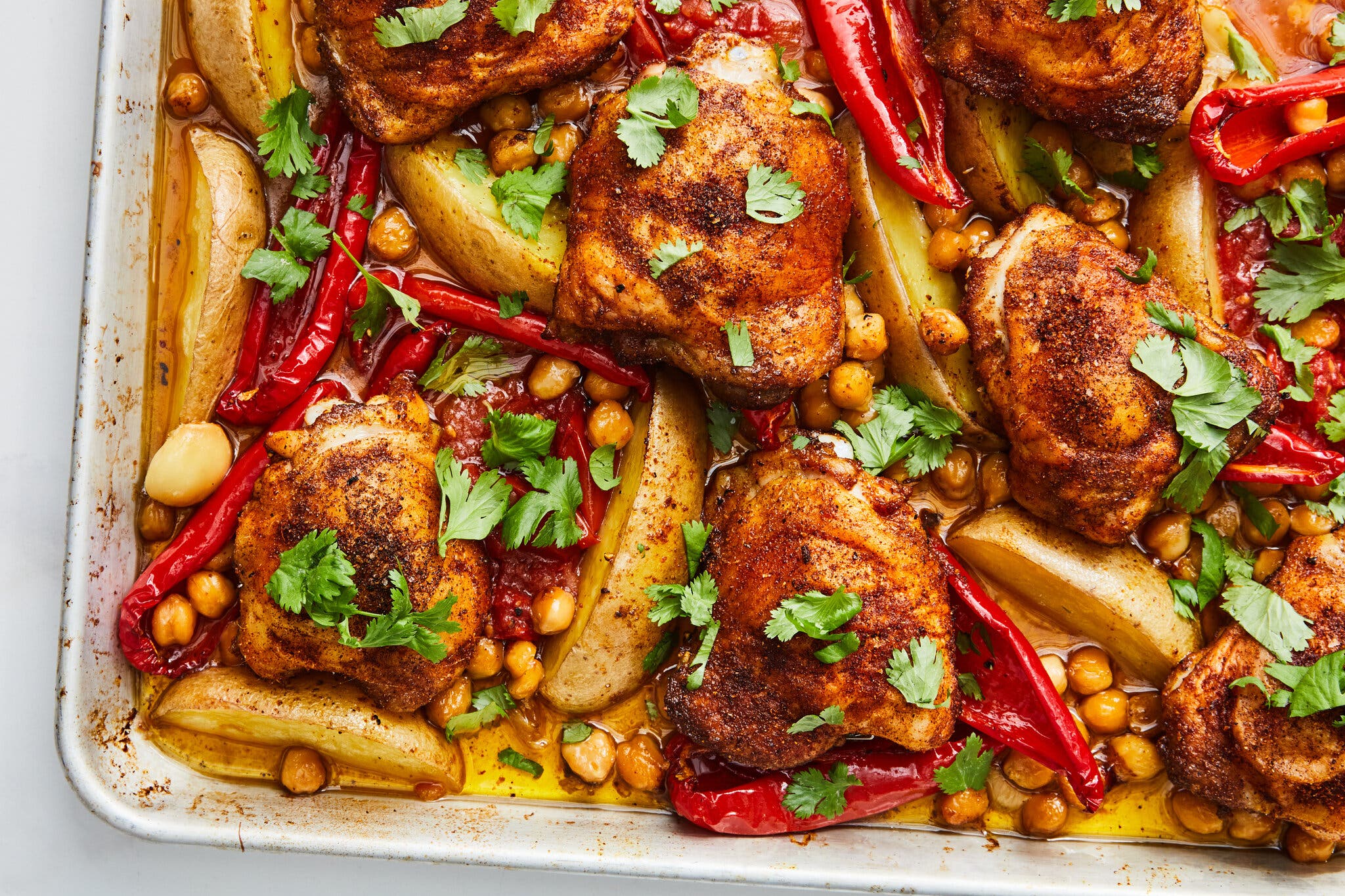 An overhead image of a sheet pan topped with cooked chicken thighs, potatoes and chickpeas.