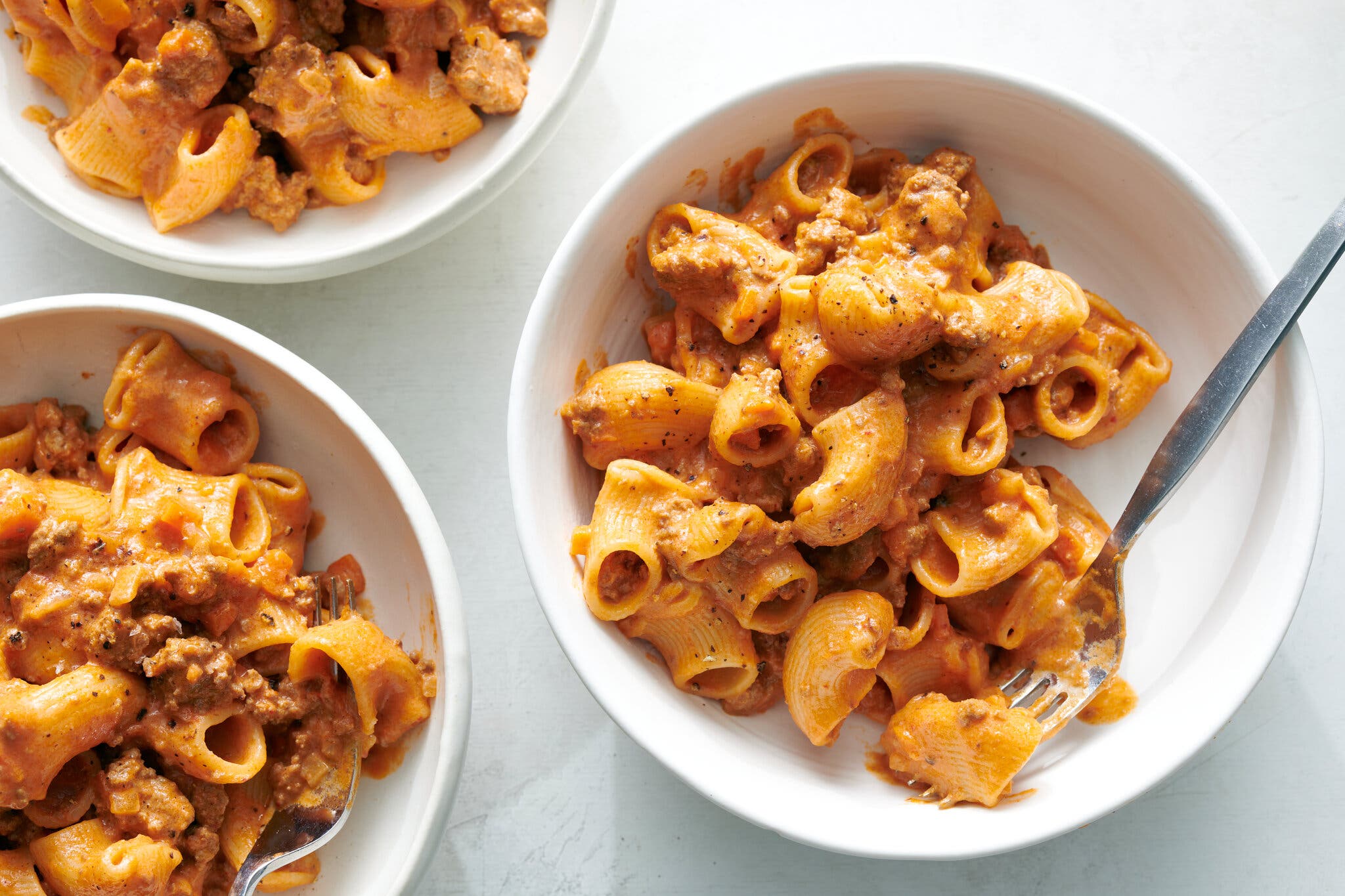 An overhead image of three bowls filled with creamy bolognese-sauced short pasta.