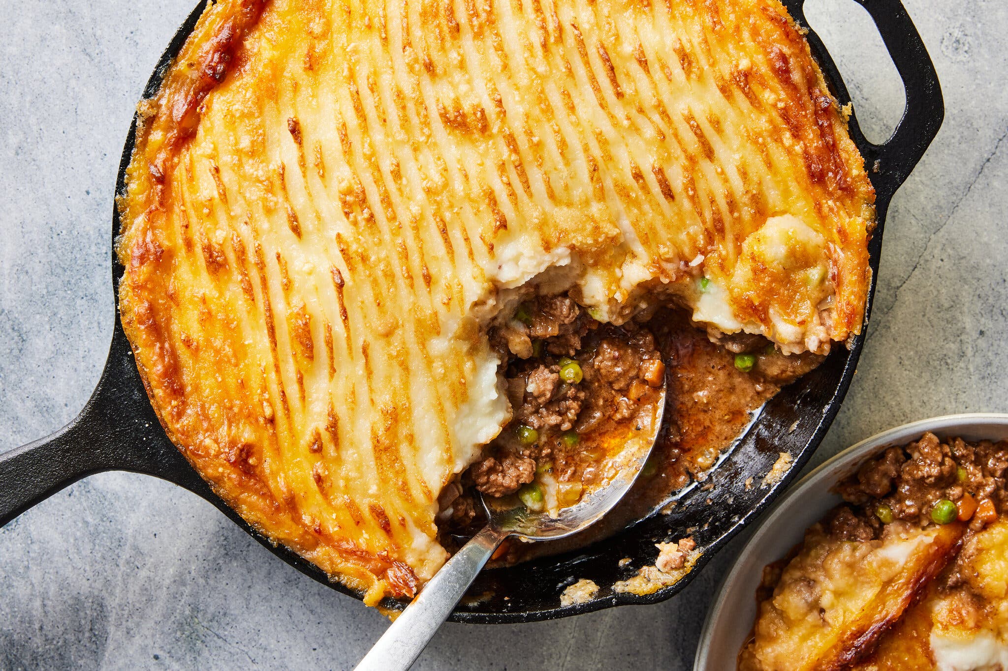 An overhead image of a cast-iron skillet topped with golden brown mashed potatoes covering a ground meat filling.