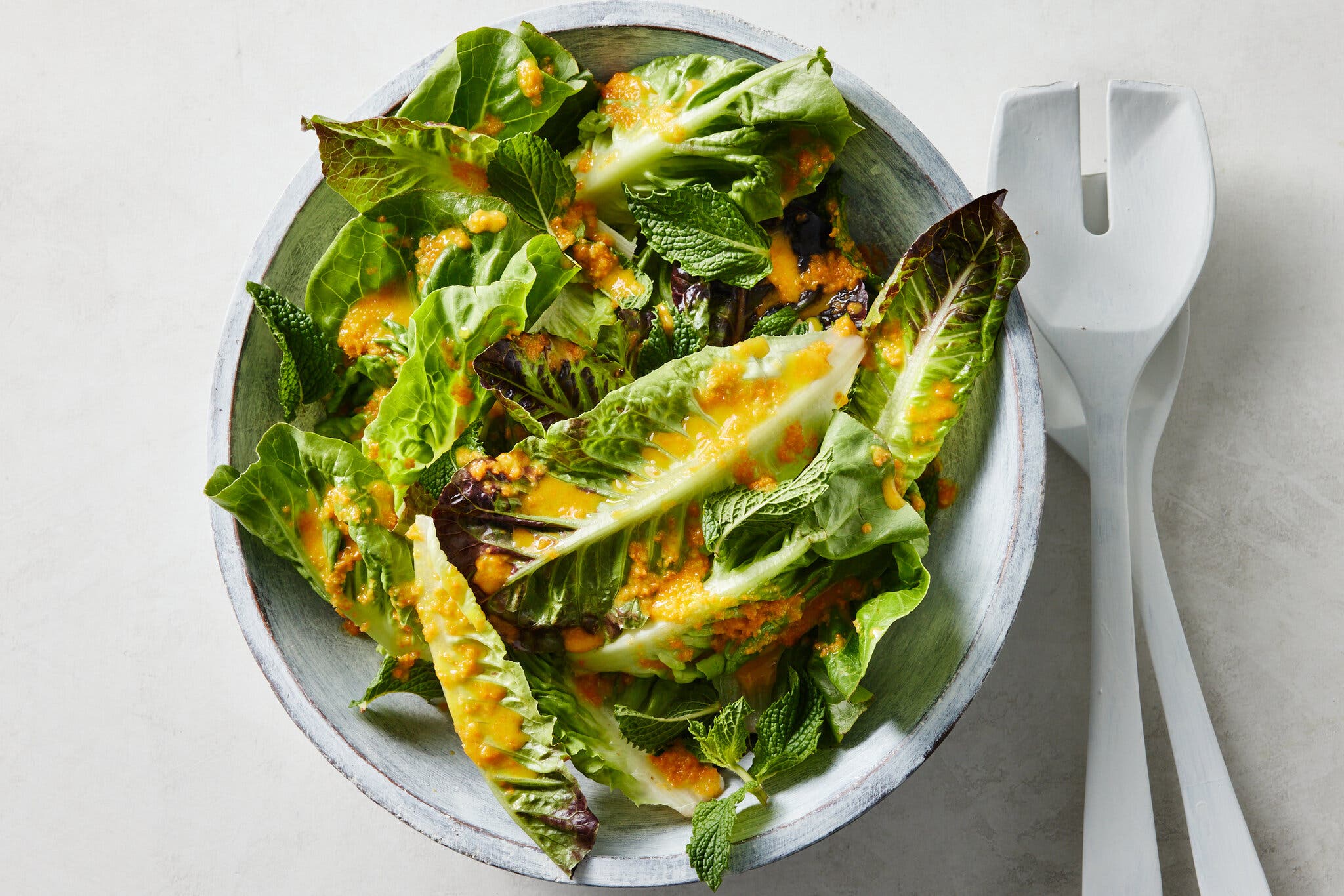 An overhead image of a large bowl of lettuce topped with an orange dressing.