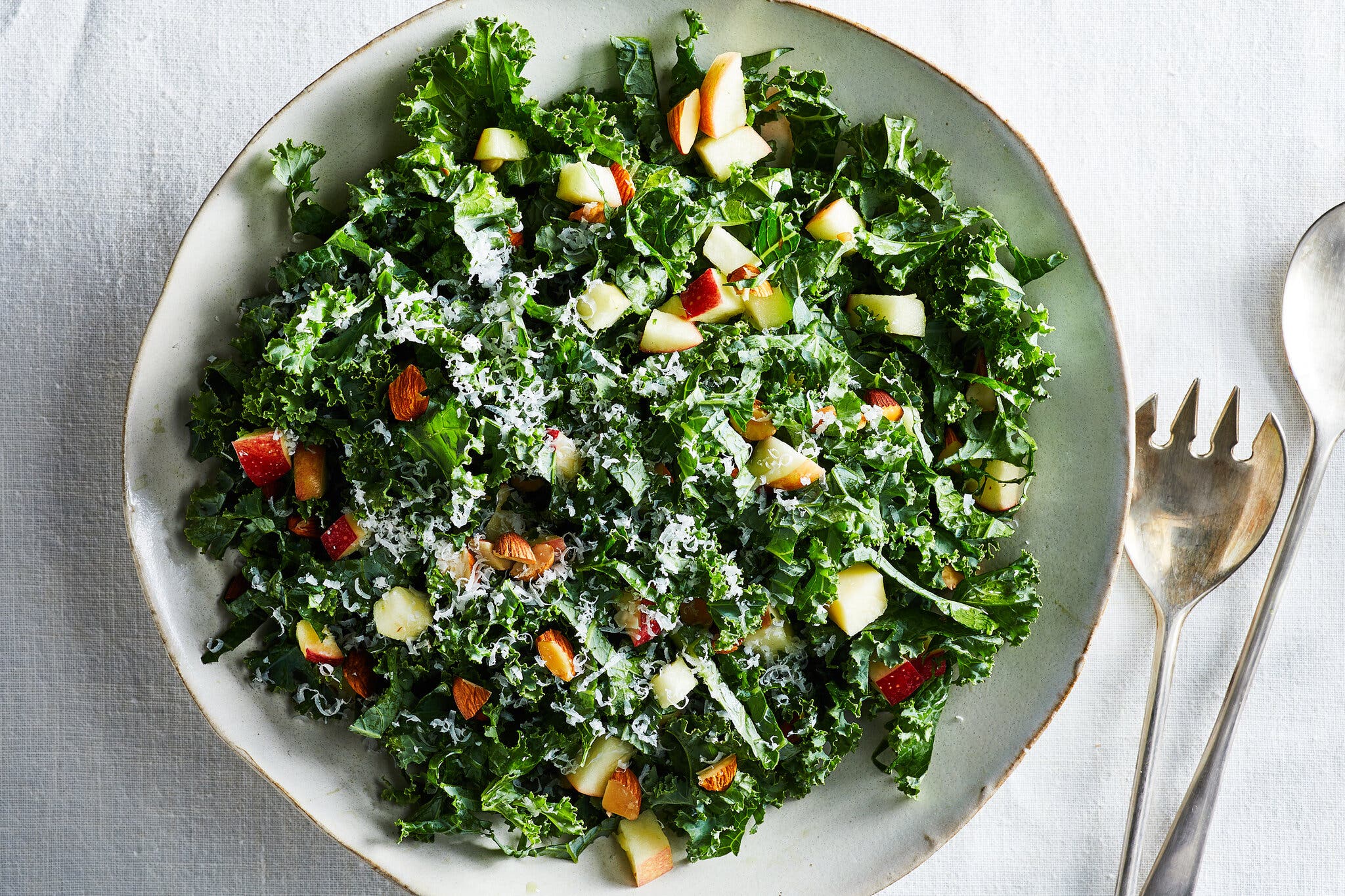 An overhead image of a kale salad topped with shredded cheese and small chunks of apple.