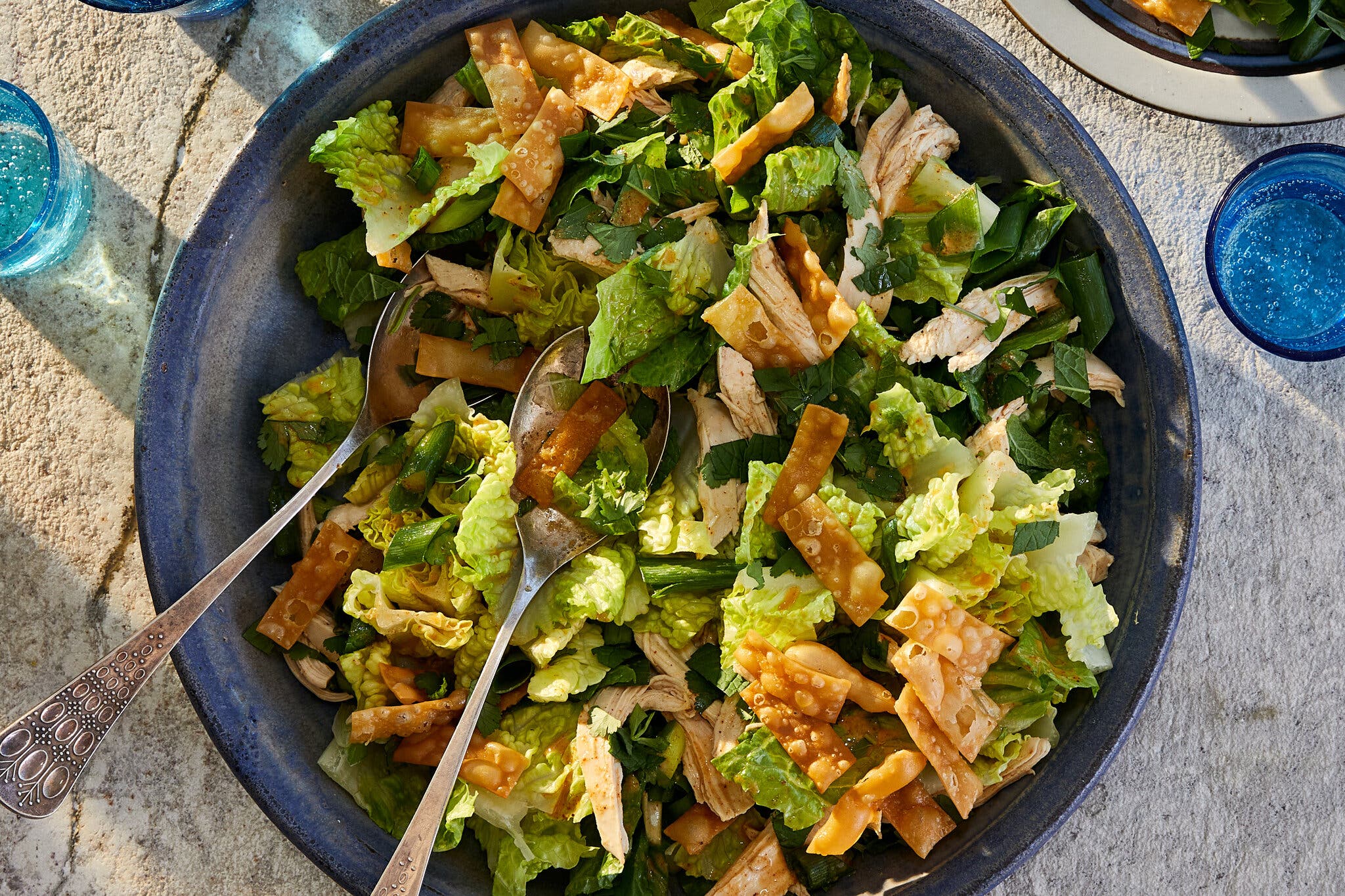 An overhead image of a bowl filled with shredded lettuce, chicken and wontons.