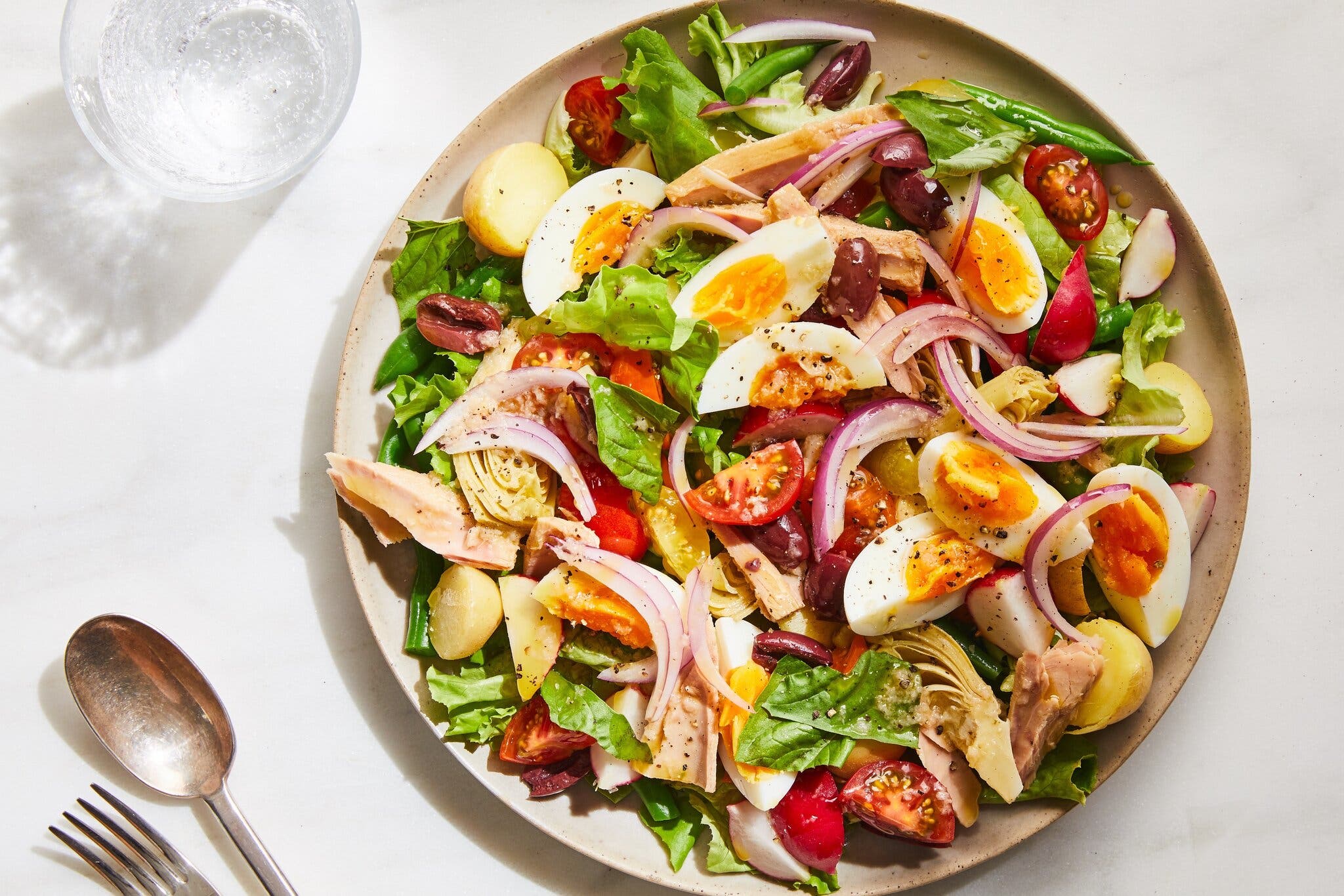 An overhead image of a platter of salad topped with greens, potatoes, onions, egg and artichoke.