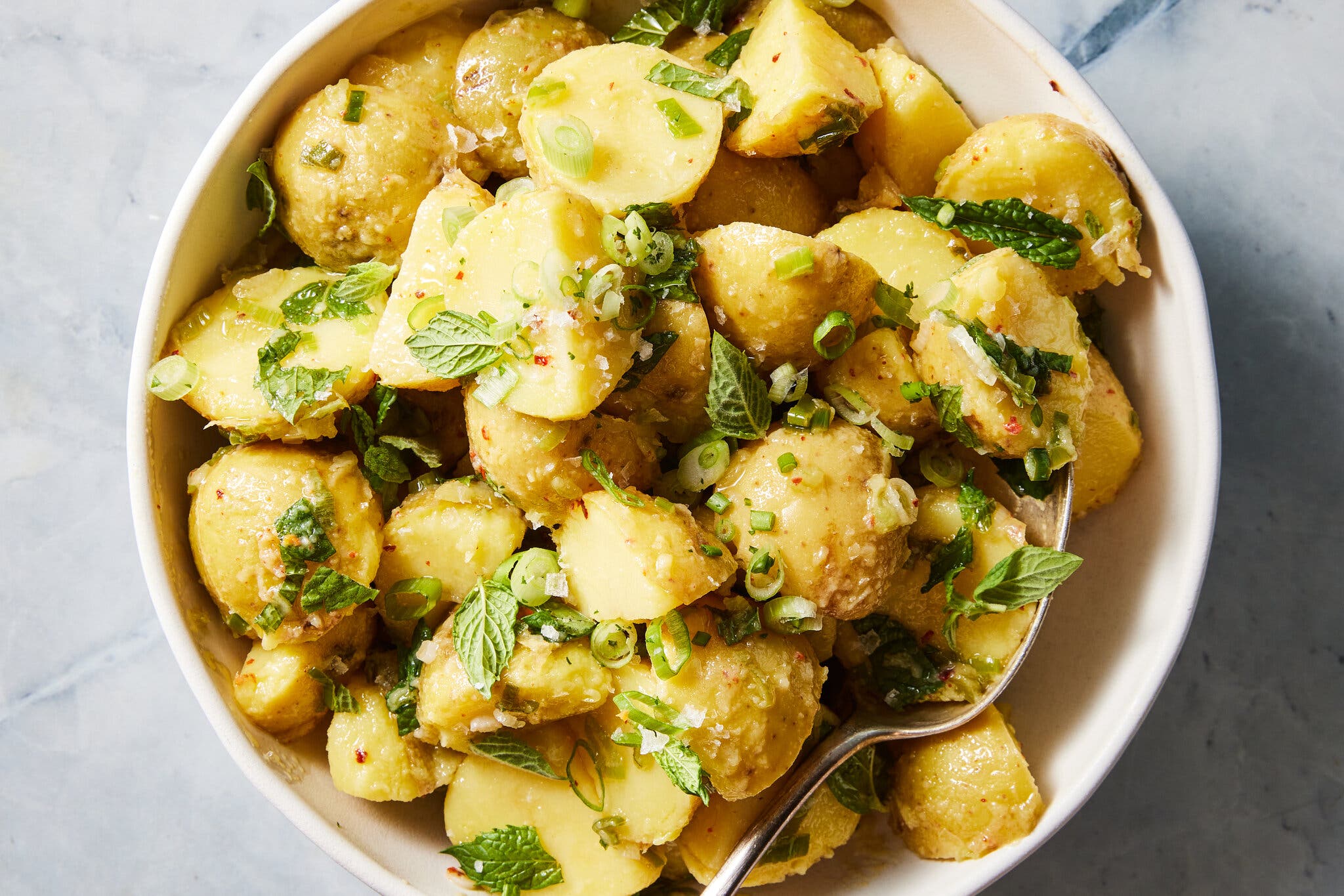 An overhead image of a bowl filled with potato salad topped with herbs.