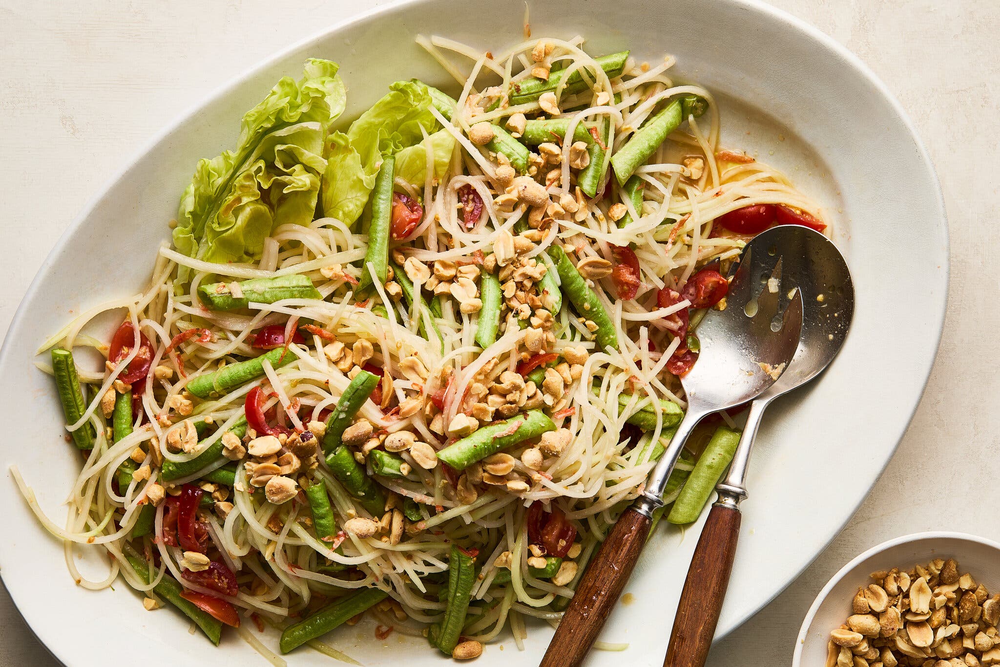 An overhead image of shredded papaya, green beans and nuts on a white platter.