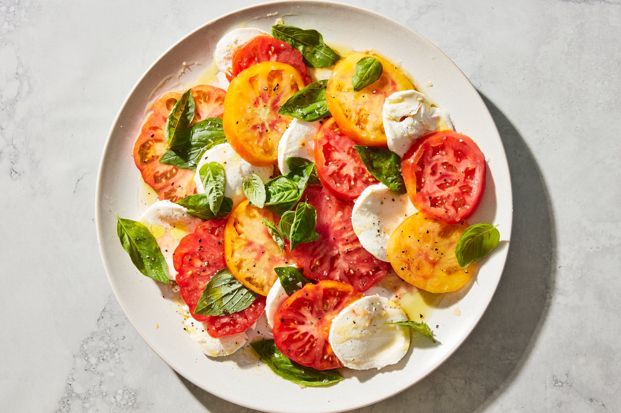 An overhead image of sliced tomatoes and mozzarella arranged artfully on a platter and topped with basil leaves.