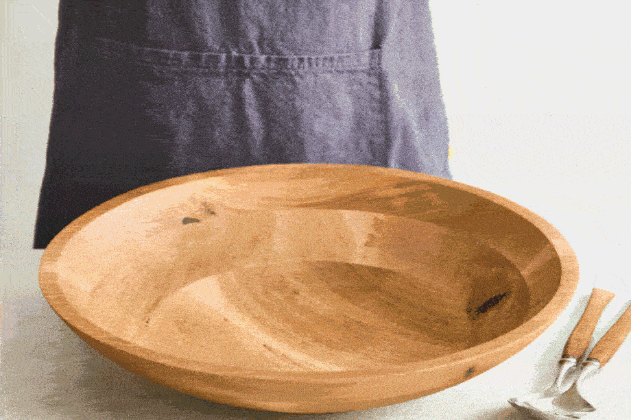 An image of a person in an apron tossing salad in a wooden bowl.
