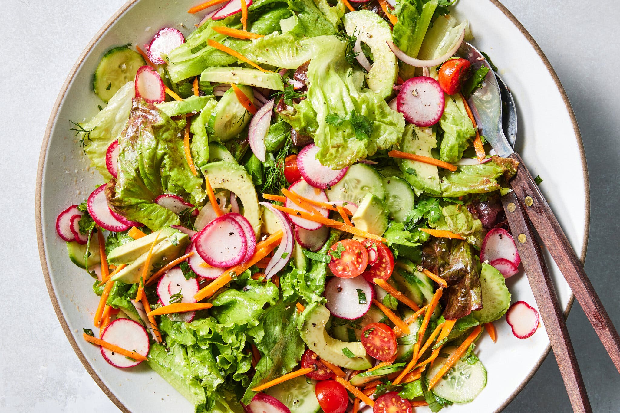 An overhead image of a large bowl of green salad topped with sliced radishes, halved tomatoes and avocado.
