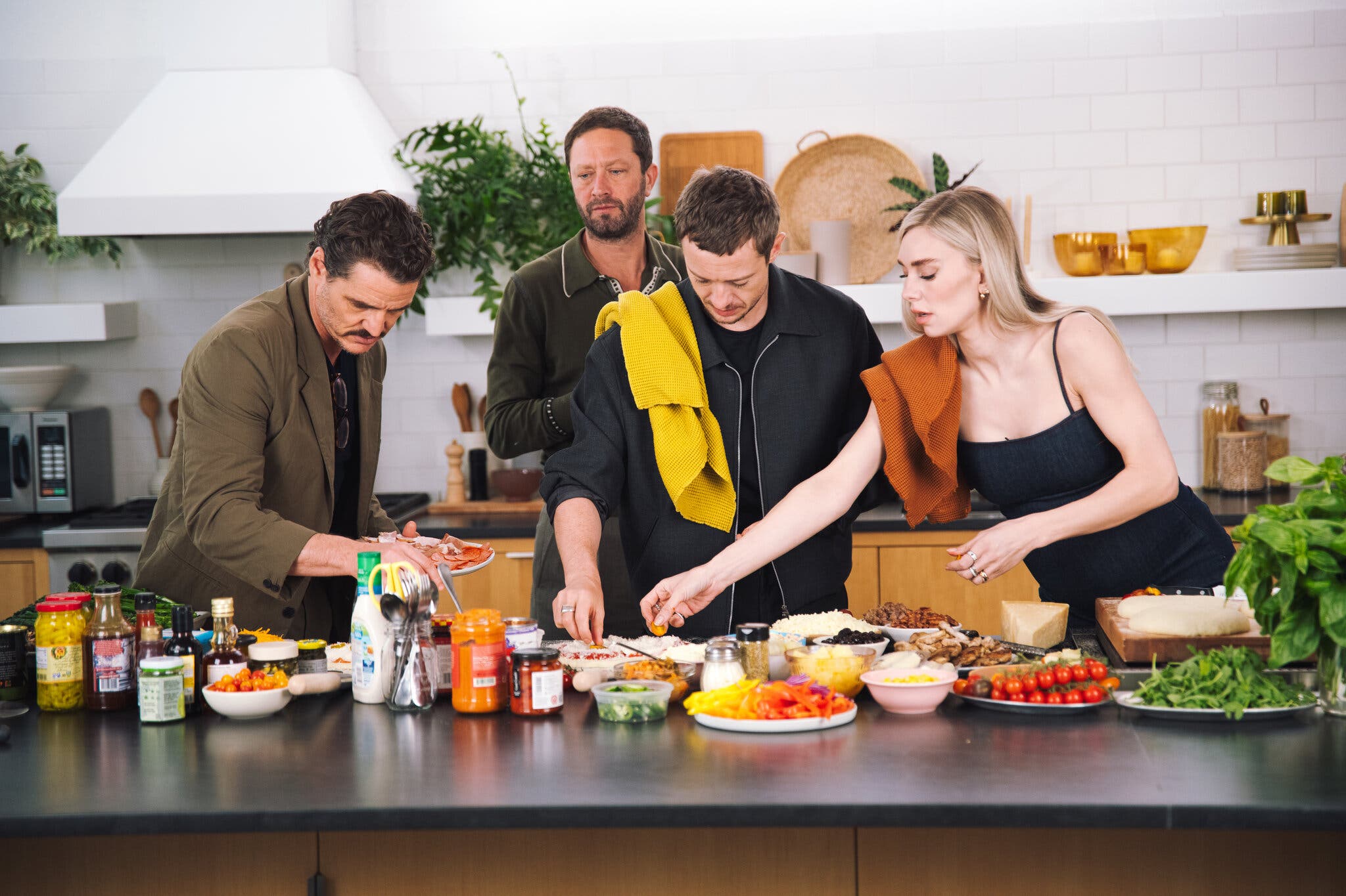An image of four people at a kitchen counter topped with all kinds of pizza toppings.