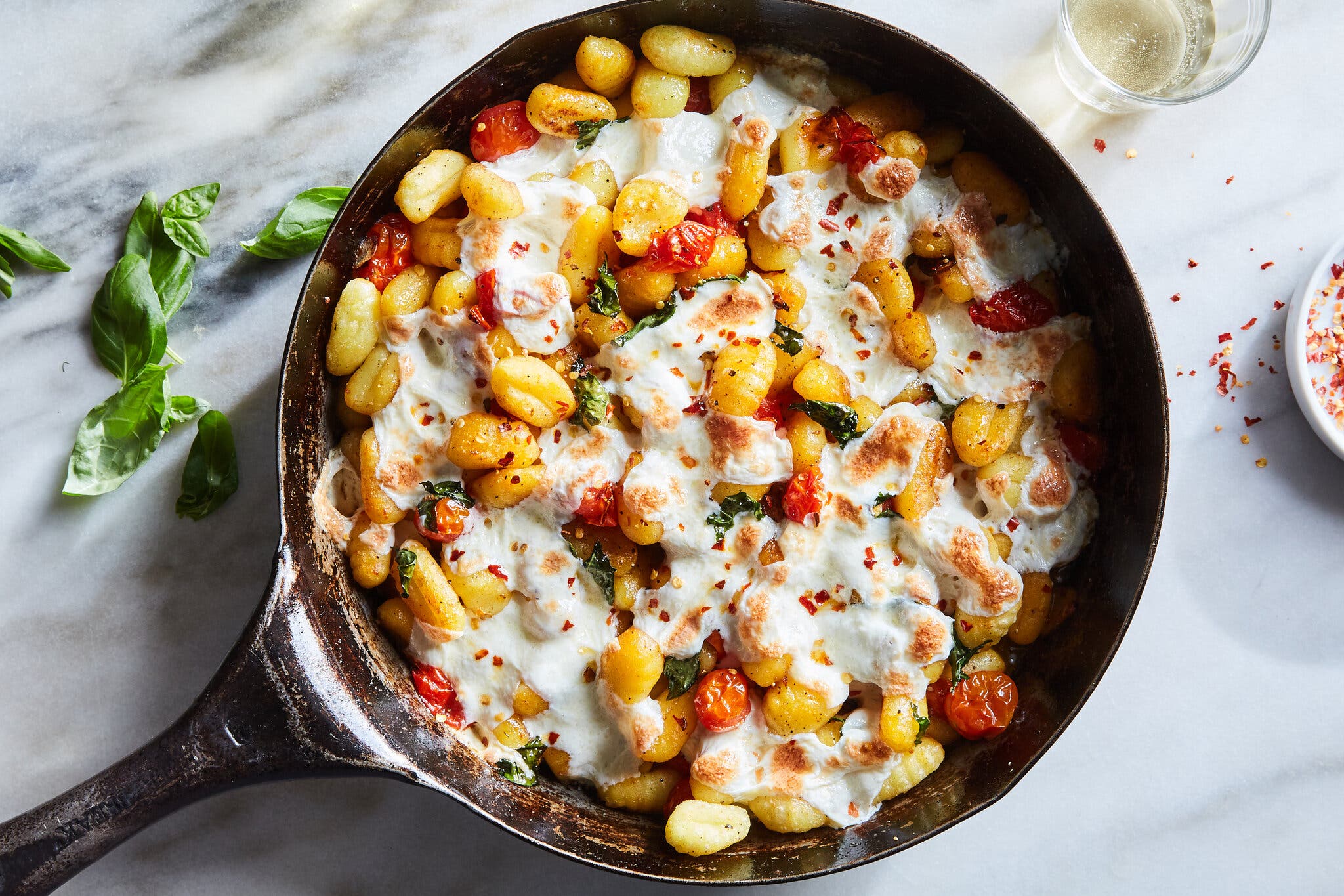 An overhead image of crisp gnocchi and tomatoes topped with mozzarella in a cast-iron skillet.