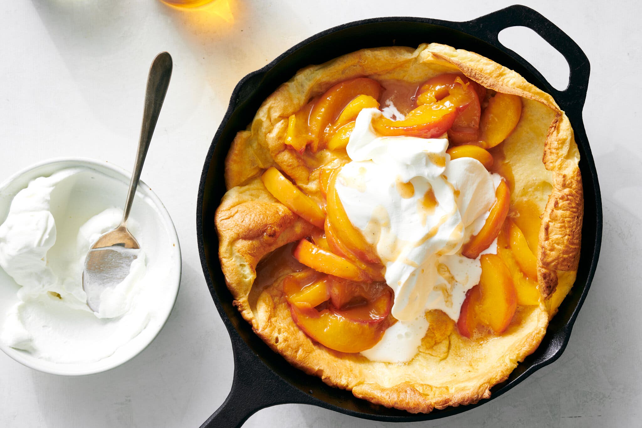 A Dutch baby pancake topped with caramelized peaches and whipped cream in a cast-iron skillet.