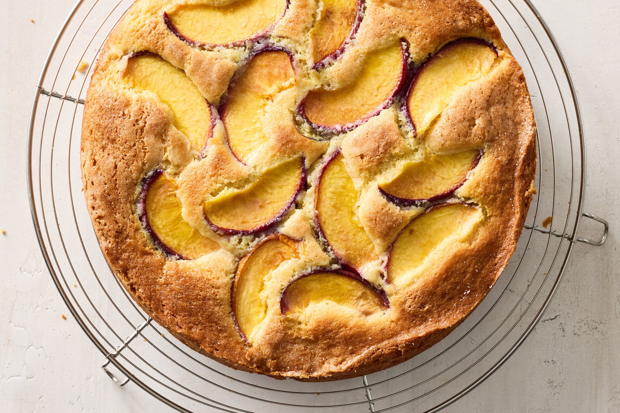 A round, golden cake with sliced peaches baked into it, on a cooling rack.