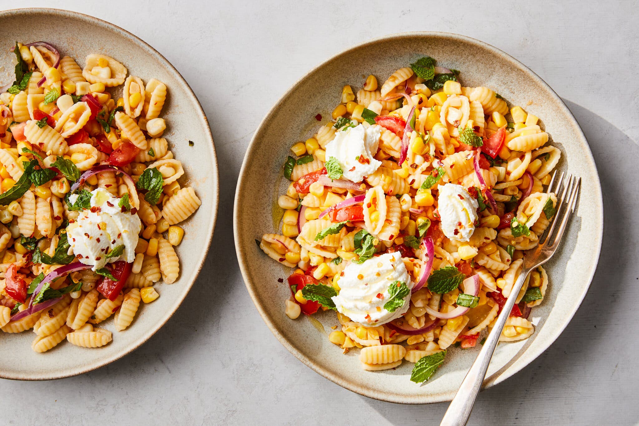 An overhead image of two bowls filled with pasta, topped with ricotta and red onion slices.